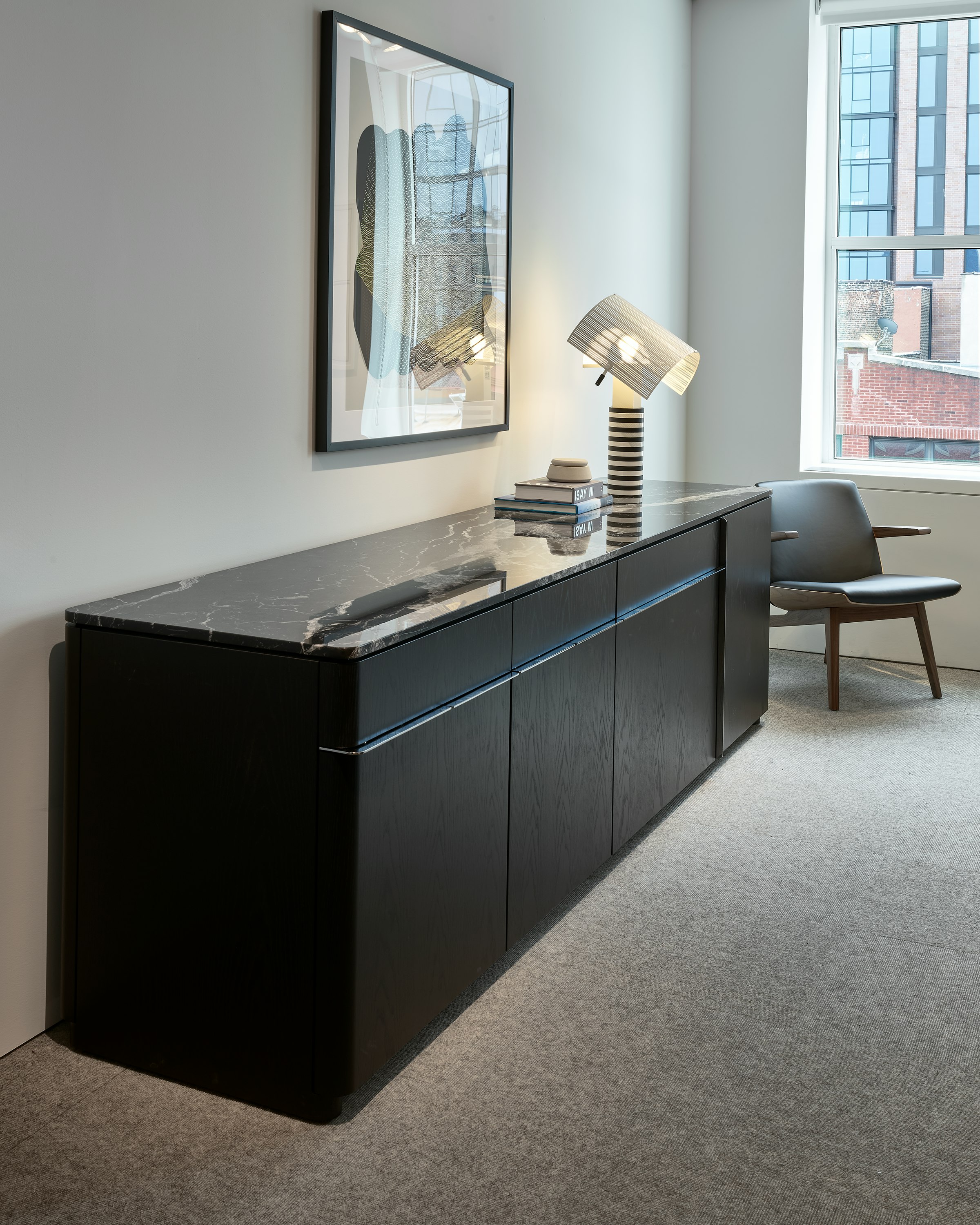 Ascent Credenza designed by EOOS in Ebonized Flat Cut  Ash with a Nero Marquina Marble Top beside a Clasmshell Lounge Chair in Walnut and black leather, viewed at an angle in a conference room setting.