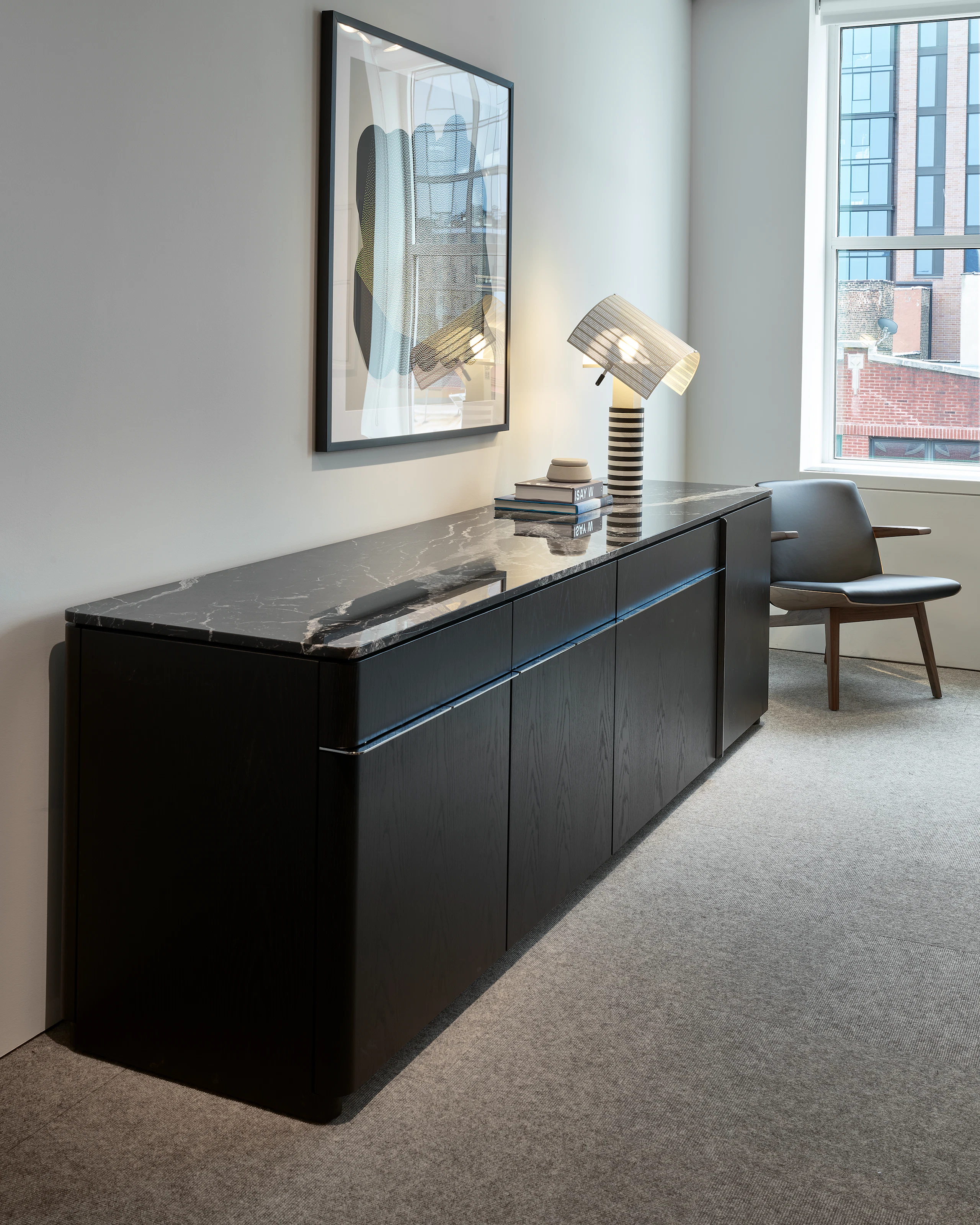 Ascent Credenza designed by EOOS in Ebonized Flat Cut Ash with a Nero Marquina Marble Top beside a Clasmshell Lounge Chair in Walnut and black leather, viewed at an angle in a conference room setting.