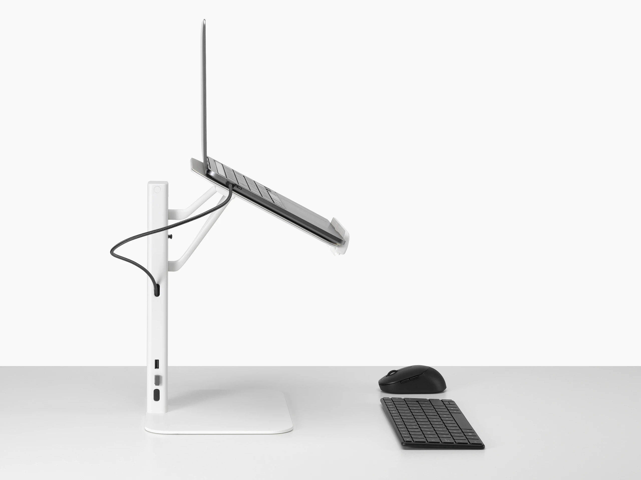 Lana laptop stand with laptop keyboard and mouse in white viewed from the side.