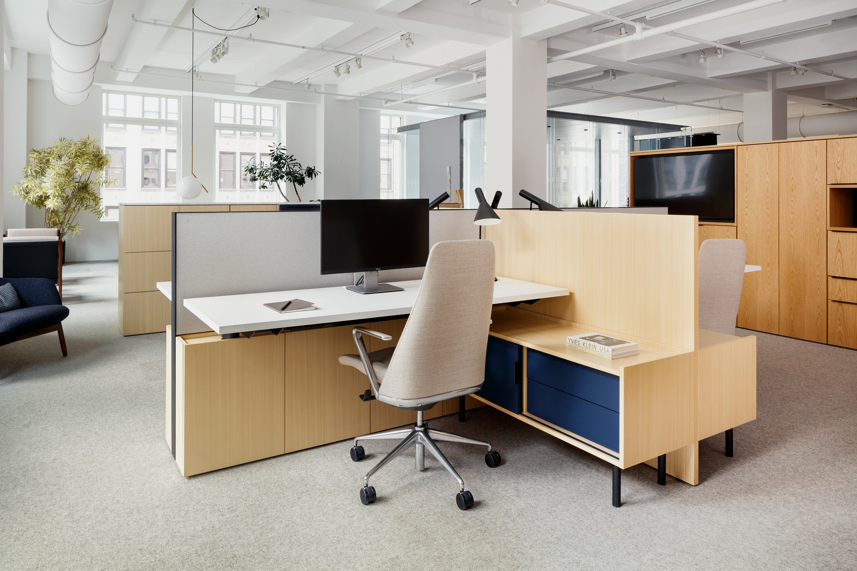 Angled view of Geiger One desk setting with white worksurfaces, light oak wood and painted medium blue storage, with back view of light beige Taper Task Chair.