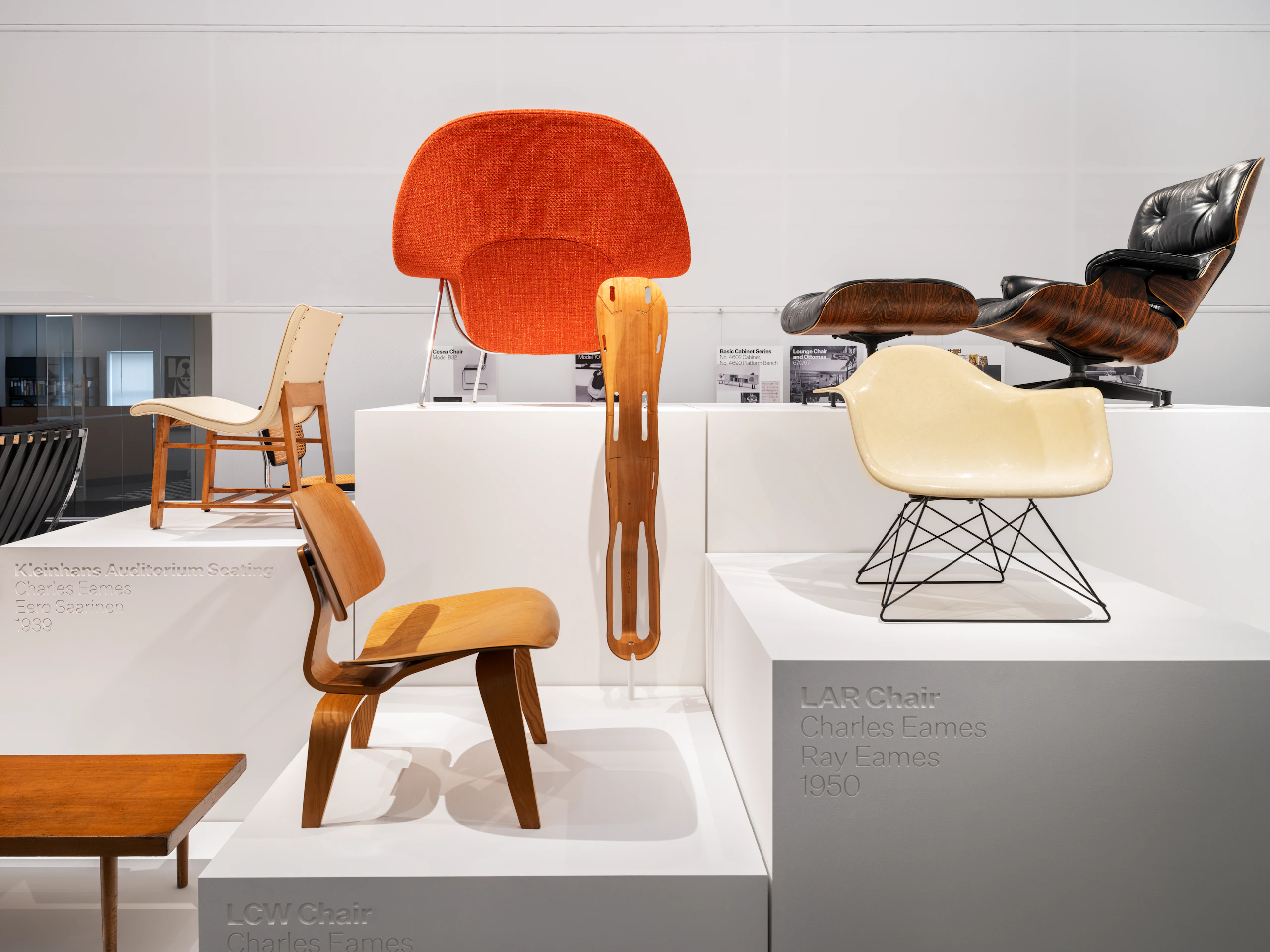 Iconic furniture pieces such as the LCW Chair, LAR Chair, Eames Lounge Chair and Ottoman, and Knoll Womb Chair on display pedestals at the MillerKnoll Archives.