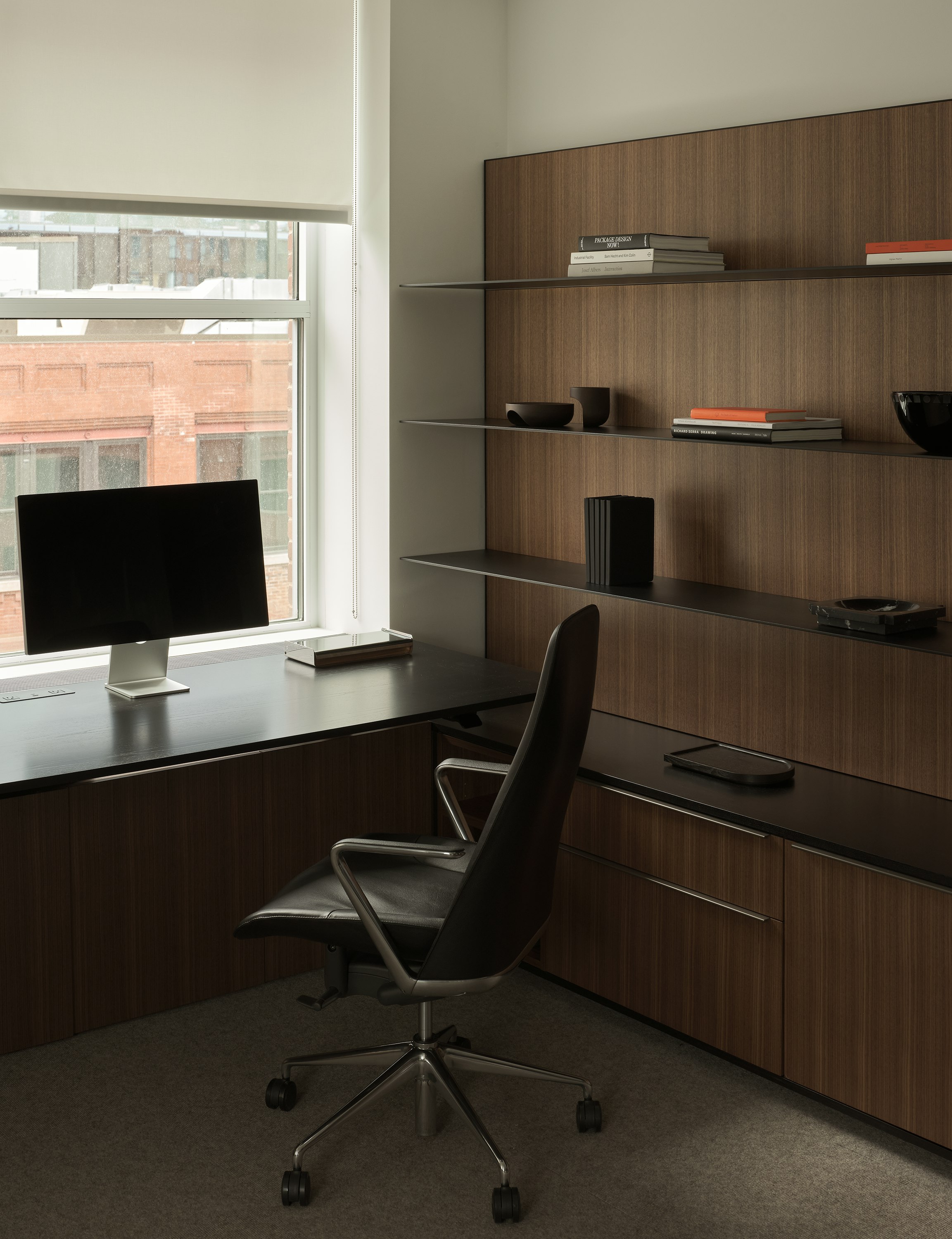 Geiger One Private Office in Natural Quarter Cut Walnut with a height-adjustable work surface in Ebonized Flat Cut Ash with black metal shelves and a Taper Chair, viewed at an angle.