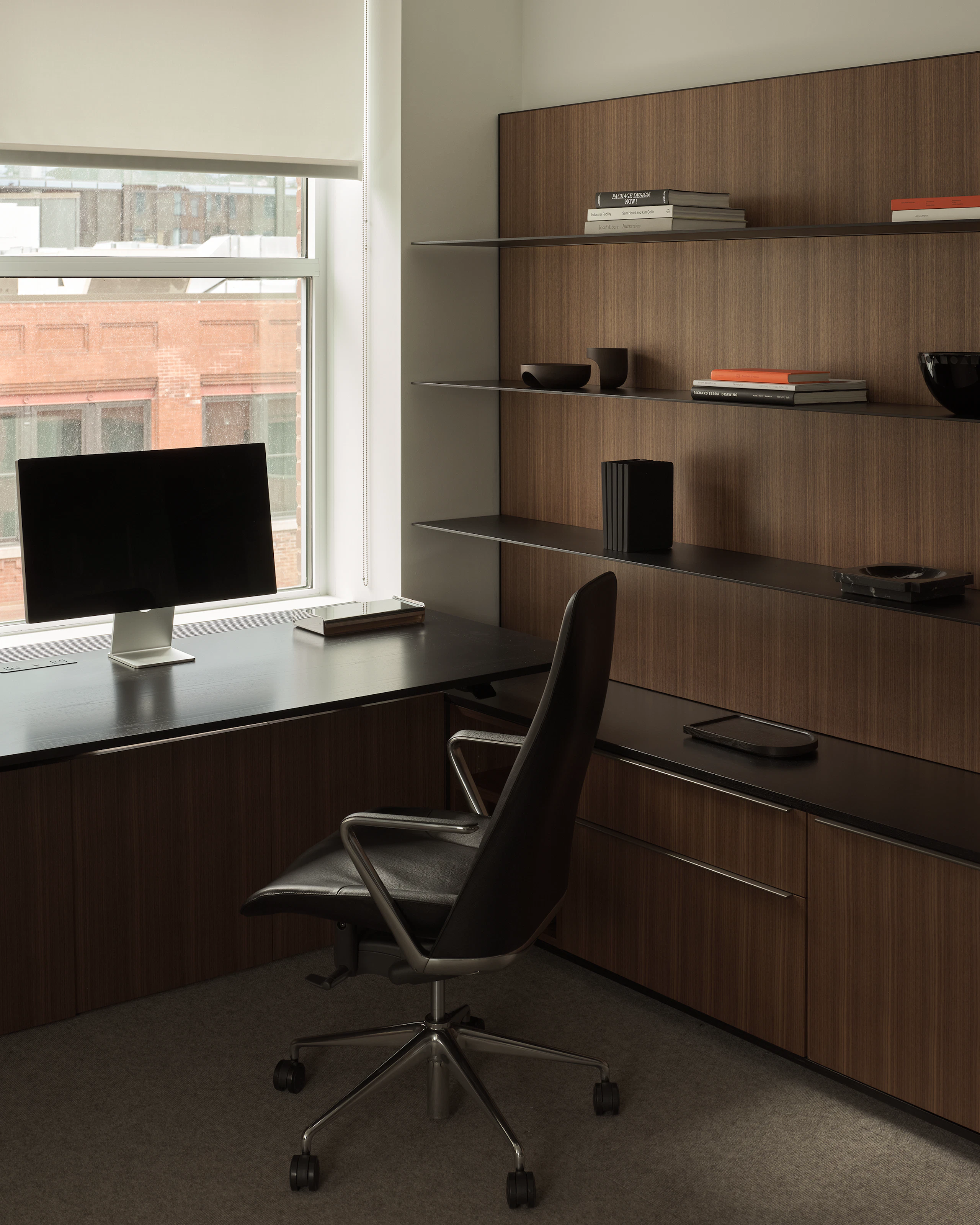 Geiger One Private Office in Natural Quarter Cut Walnut with a height-adjustable work surface in Ebonized Flat Cut Ash with black metal shelves and a Taper Chair, viewed at an angle.