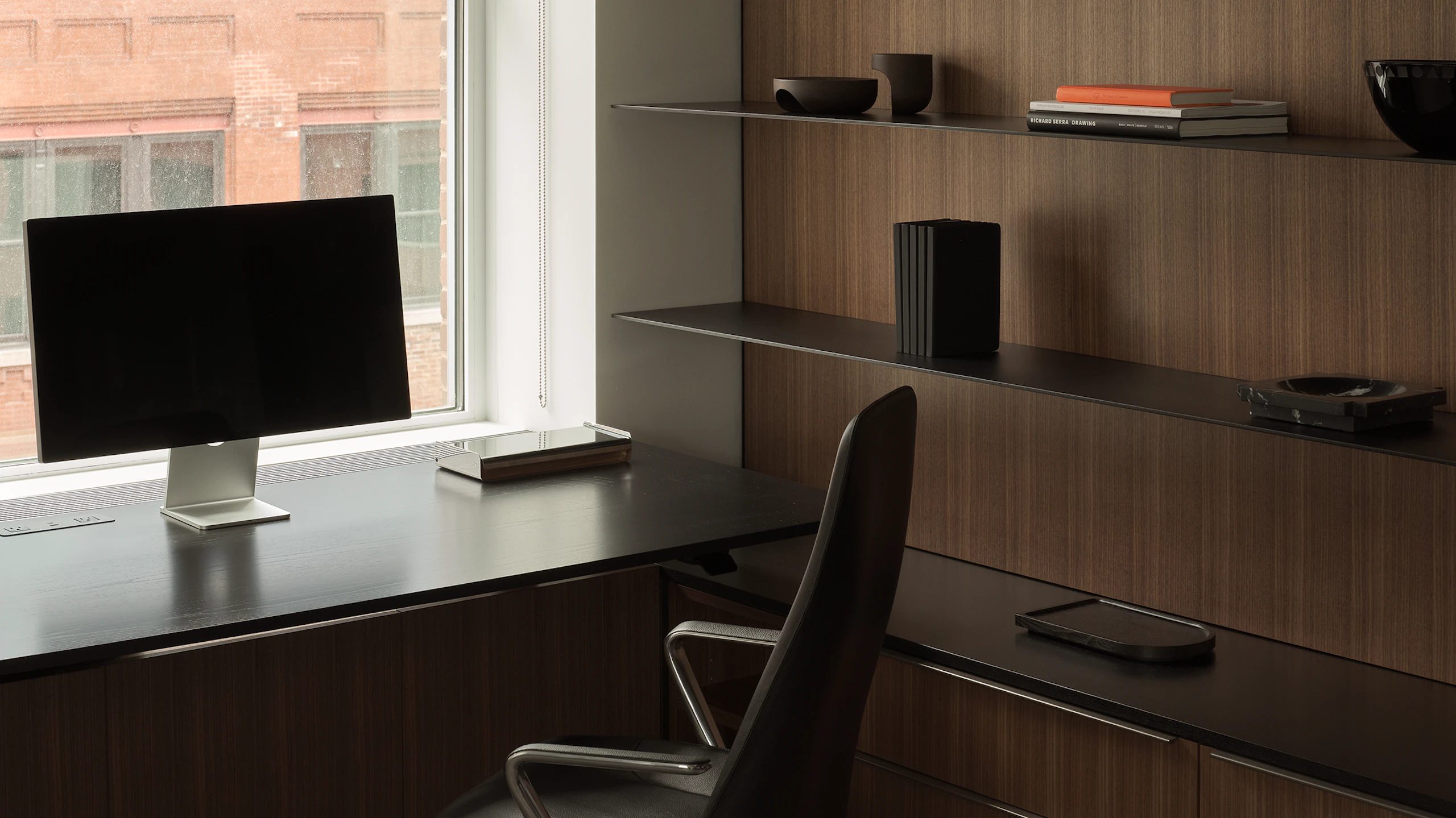Geiger One Private Office in Natural Quarter Cut Walnut with a height-adjustable work surface in Ebonized Flat Cut Ash with black metal shelves and a Taper Chair, viewed at an angle.