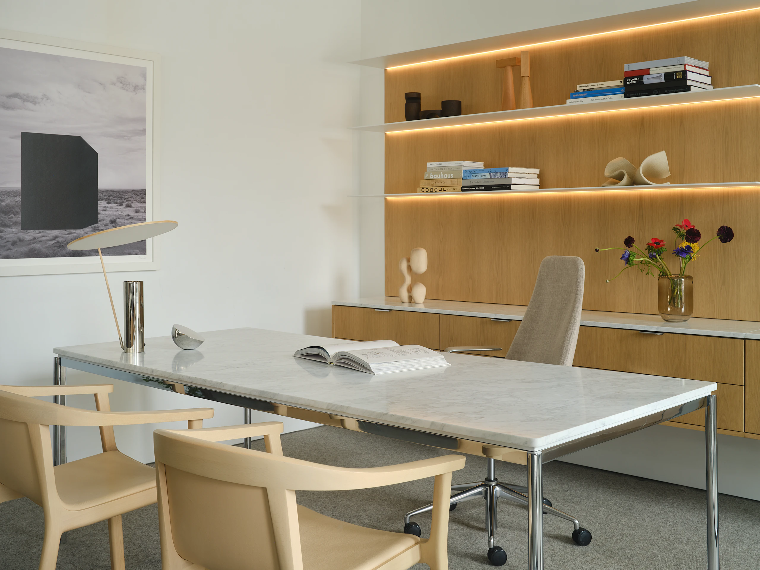 Geiger One Casegoods in Nordic Oak veneer shown at an angle with freestanding Parsons table with white marble top, Taper chair, and two Lijn Armchairs for guests in a private office setting