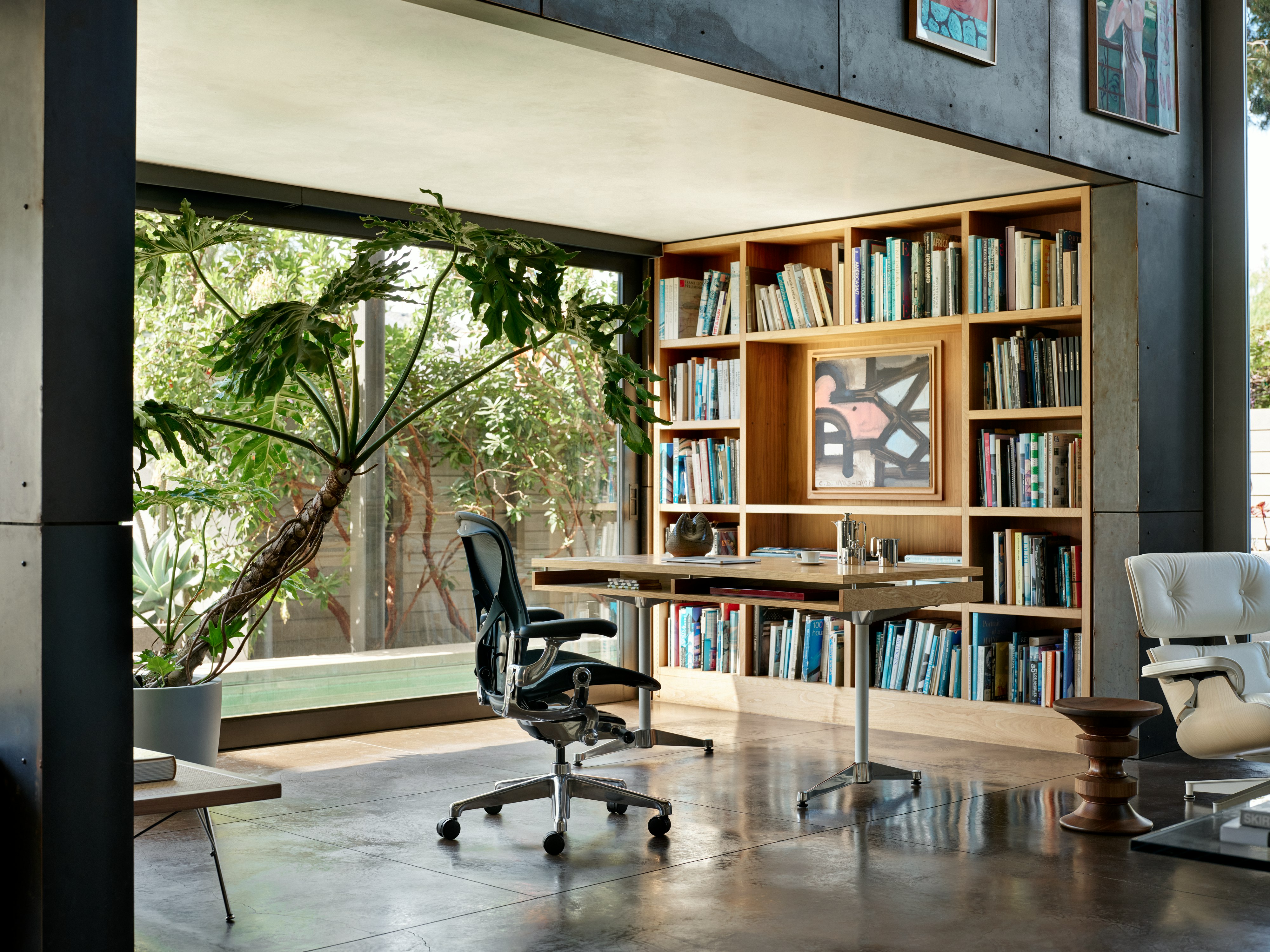 A dark blue Aeron Chair with a polished base and chassis in front of an Eames 2500 desk and bookshelf in a home office.