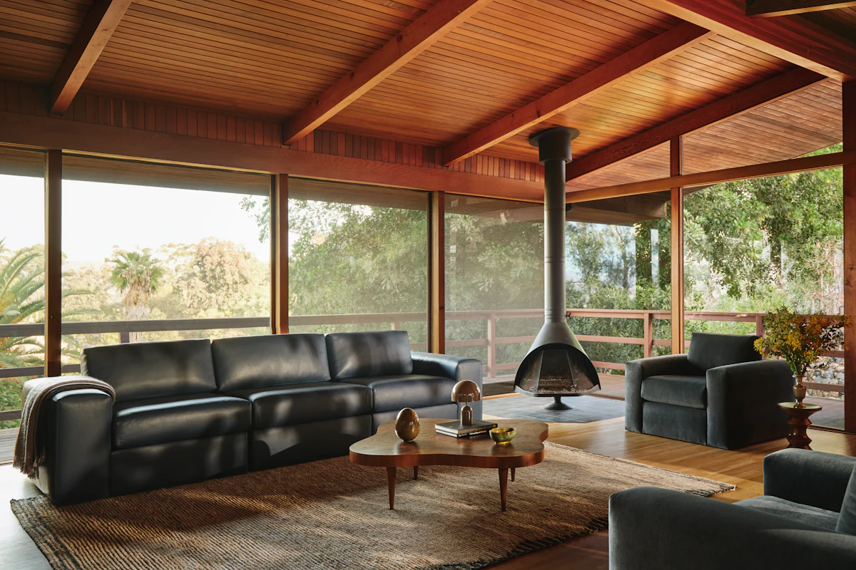 A large outdoor-like living space with black leather sofas, a fireplace, and wooden ceiling beams.