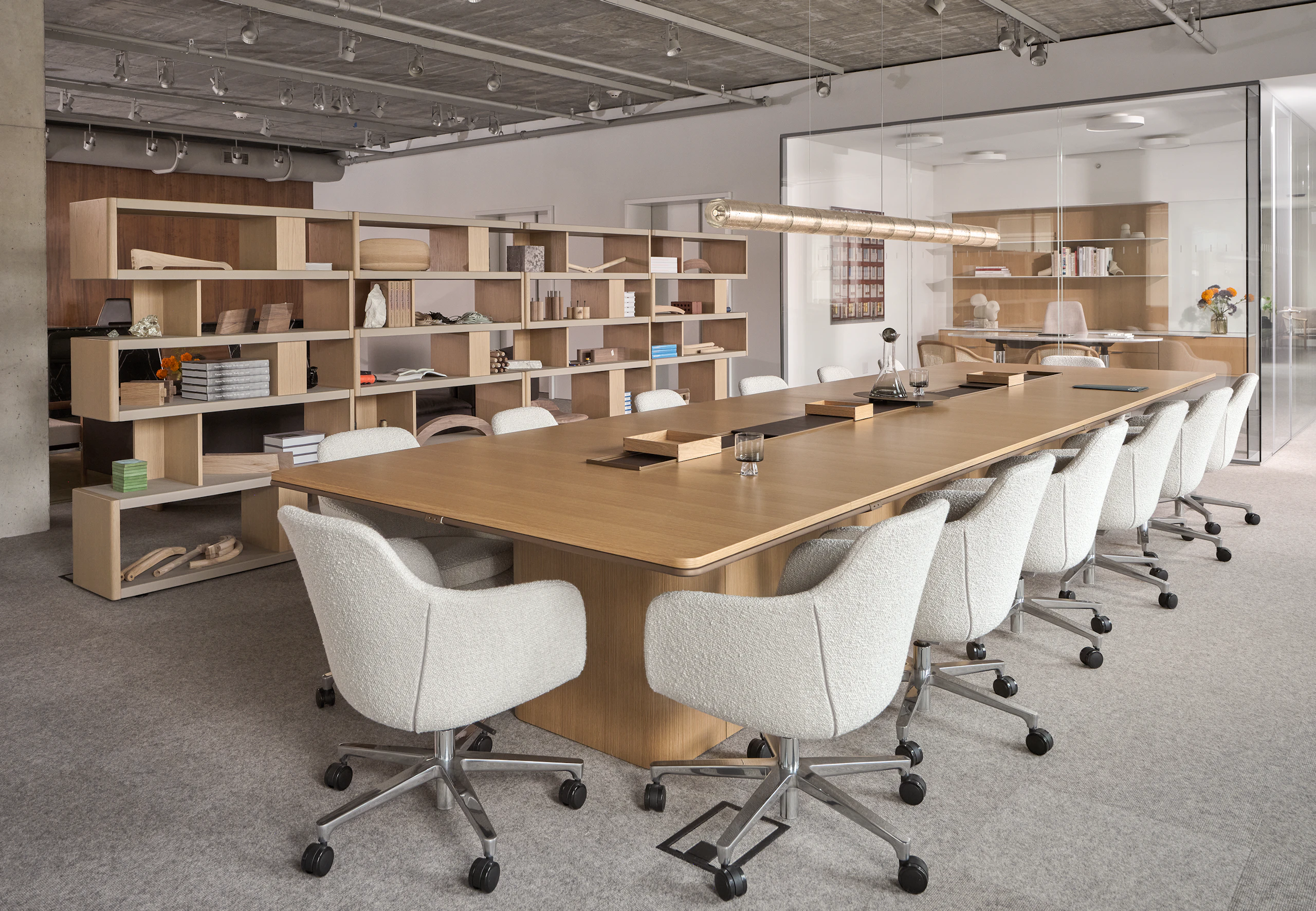 An Ascent Conference Table in Natural Rift Cut Oak with a plinth base surrounded by Saiba Conference Chairs upholstered with Pristina in Dove with New Canaan Bookshelves in the background, viewed at an angle.