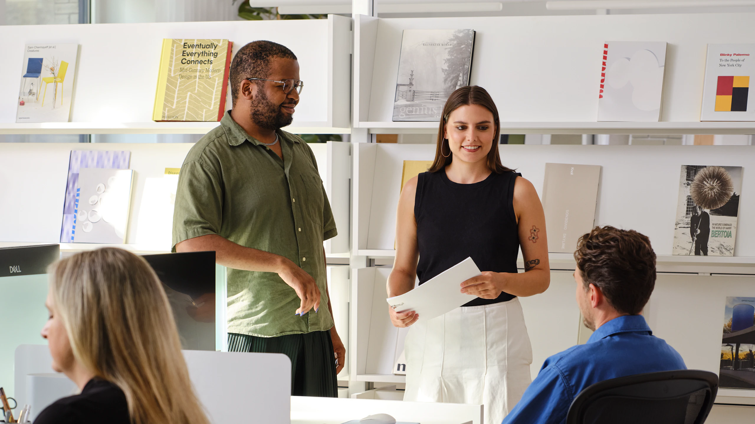 Several people having a conversation around an individual workstation furnished with Herman Miller Aeron Chairs and sit-to-stand desks.