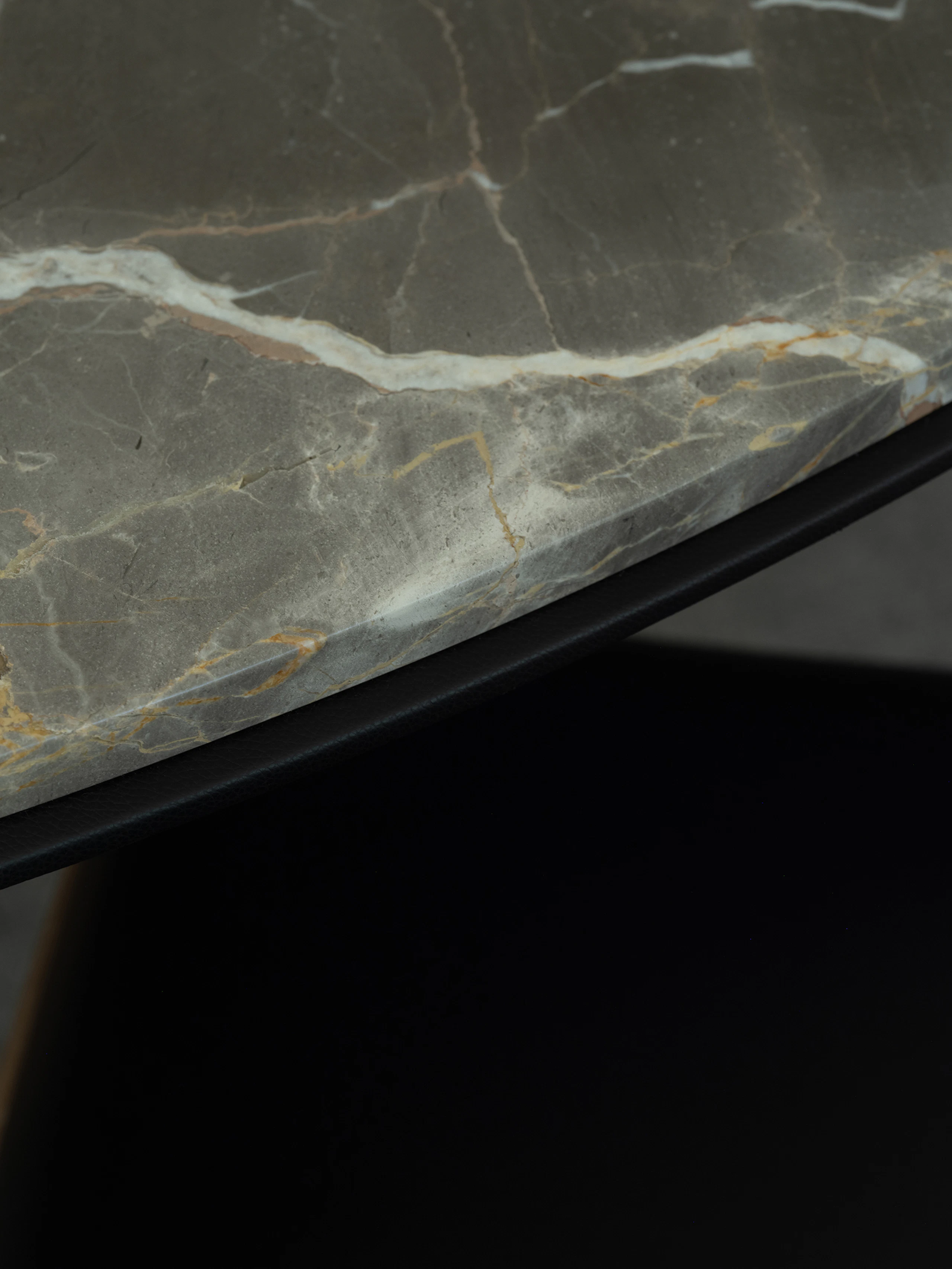 Detail view of a Highline Fifty Meeting Table edge with an Ombra di Caravaggio marble top and black leather edge, viewed at an angle.