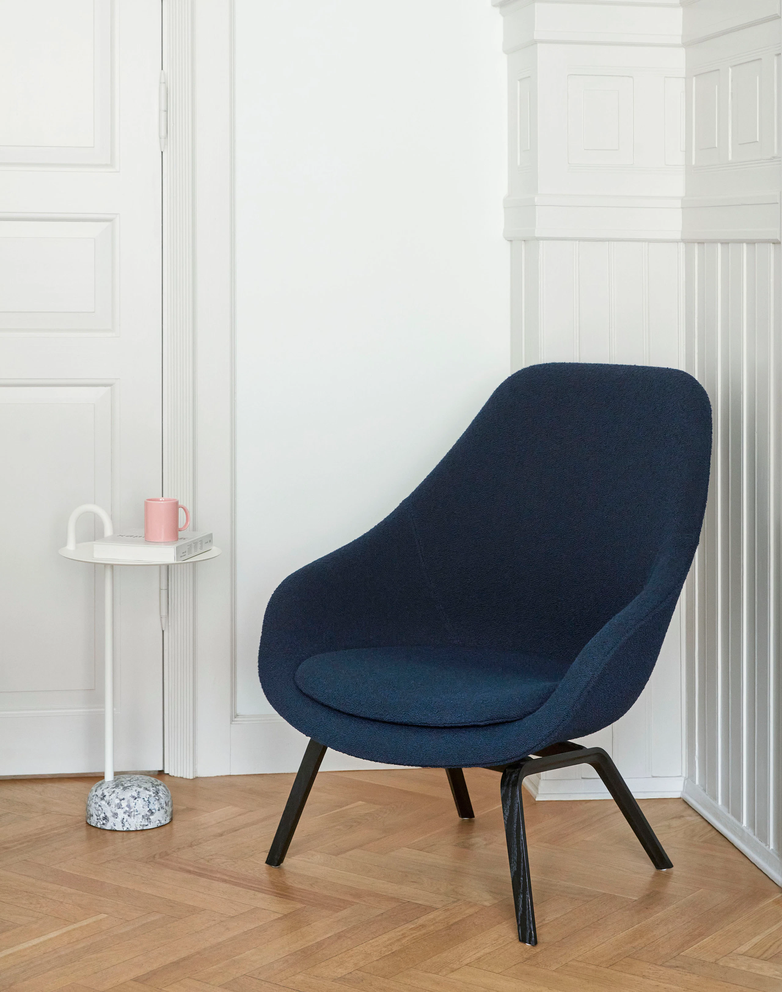 A white Bowler Table next to a navy blue About A Lounge Chair.