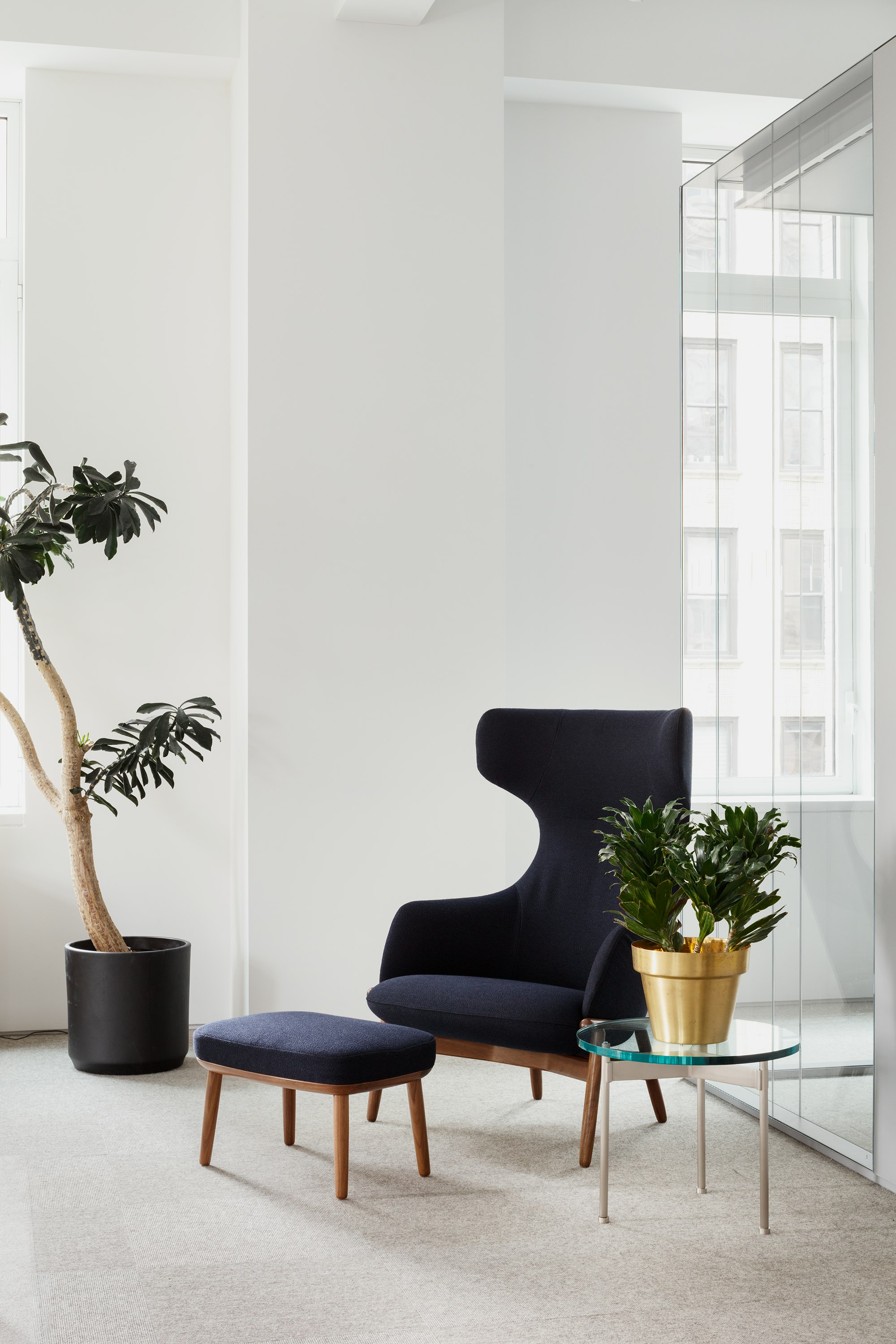 Eye level view of the Reframe Wingback Chair and Crosshatch Ottoman in dark blue with glass round side table with silver metal legs.