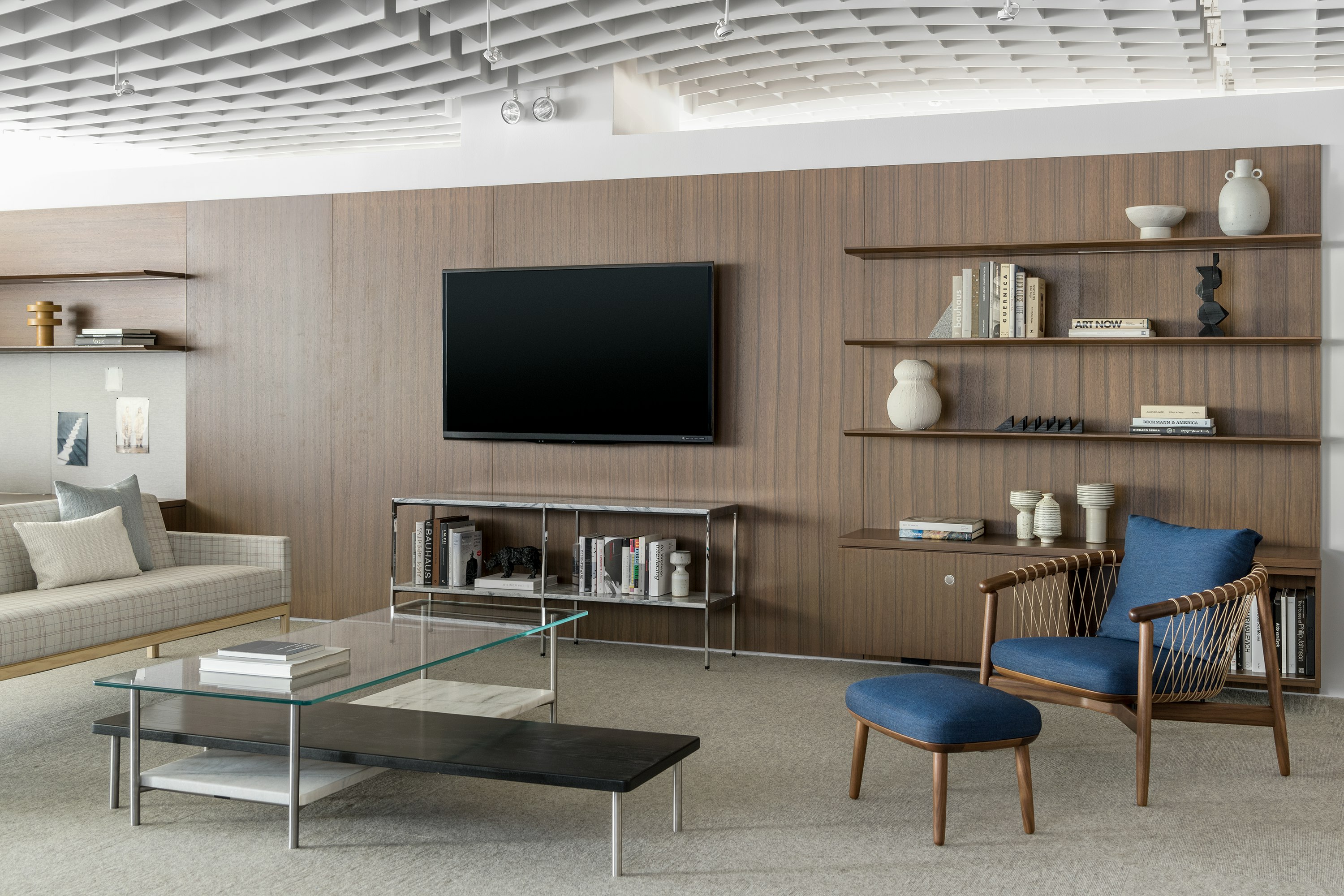 A Crosshatch Chair and Ottoman with dark blue fabric and a wood frame in a medium finish, positioned at an angle in front of bookshelves.