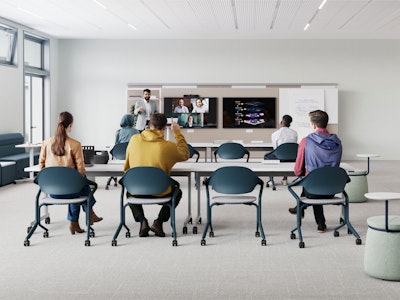 Modern classroom with focus on collaboration. Foreground features a long white table with laptops. Background shows enclosed booths with red fabric panels and white frames, some with seating and small tables inside.