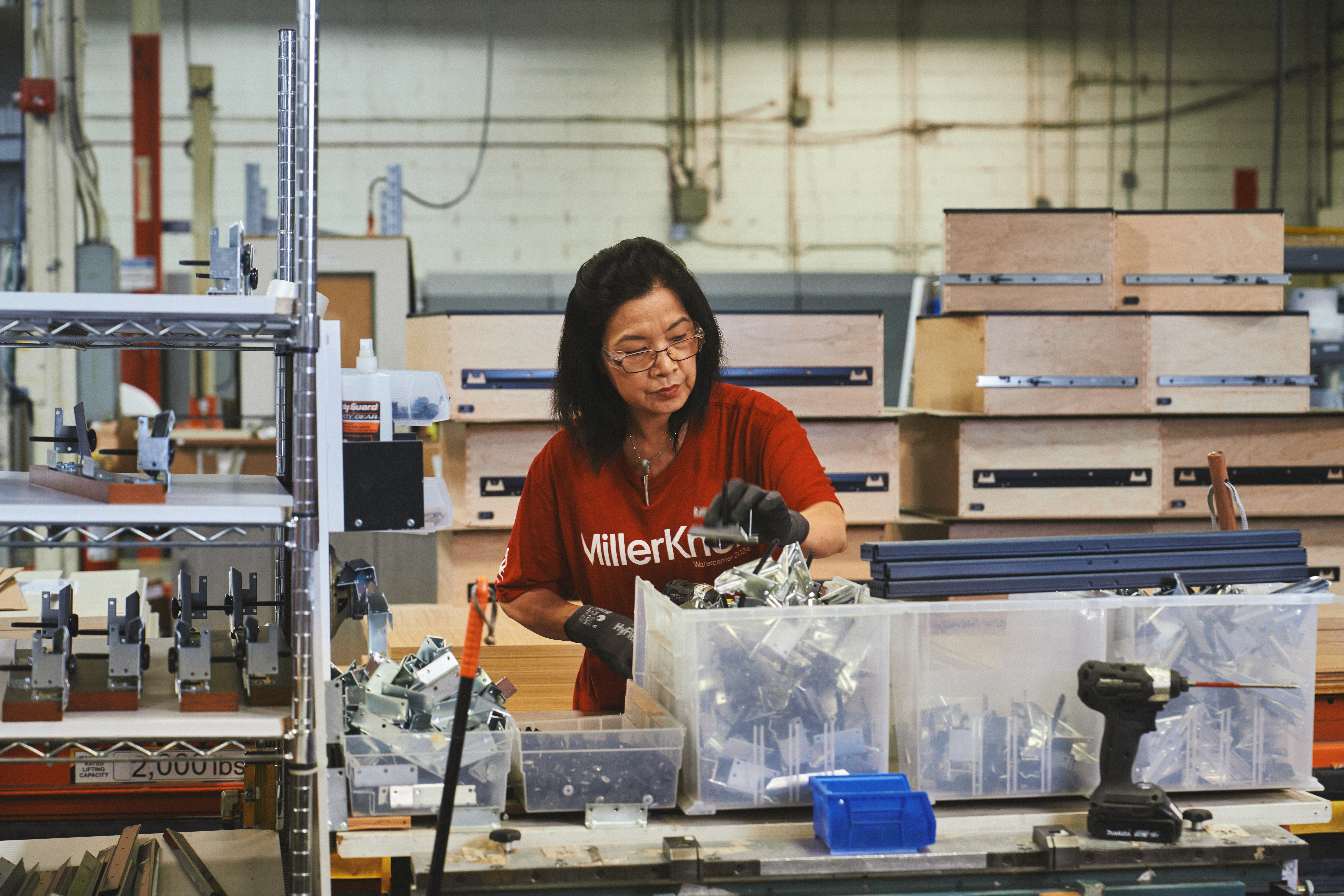 Woman in a red MillerKnoll shirt working in a manufacturing facility.