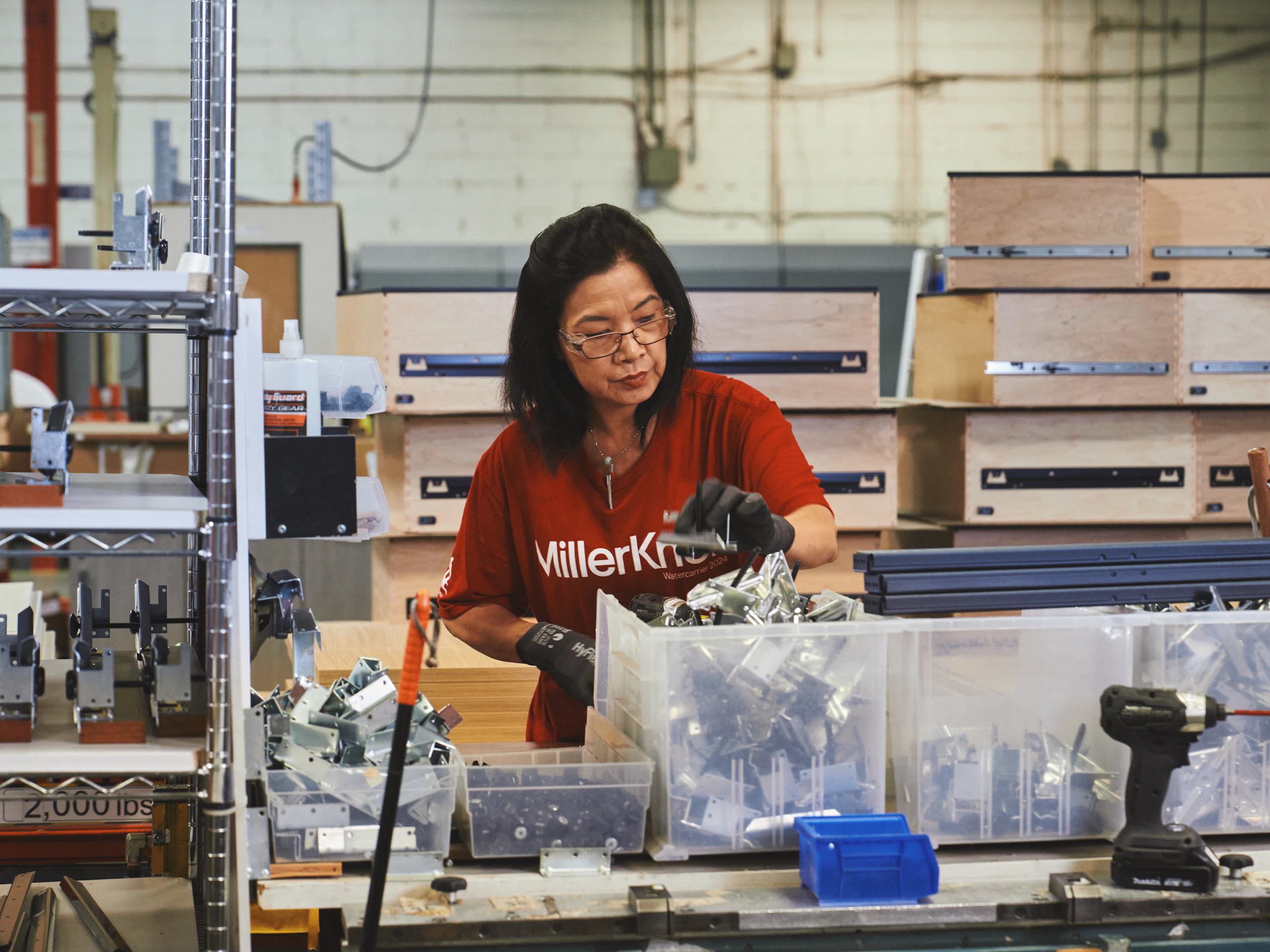 Woman in a red MillerKnoll shirt working in a manufacturing facility.