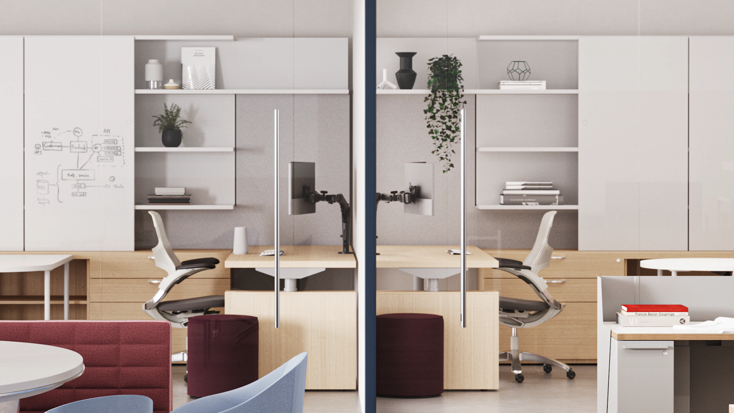 Modern workstations with white desks, pink chairs, and storage units. Glass partitions divide the space. Shelving displays plants and decorative items. Meeting area with roundtable and red sofa in the foreground.