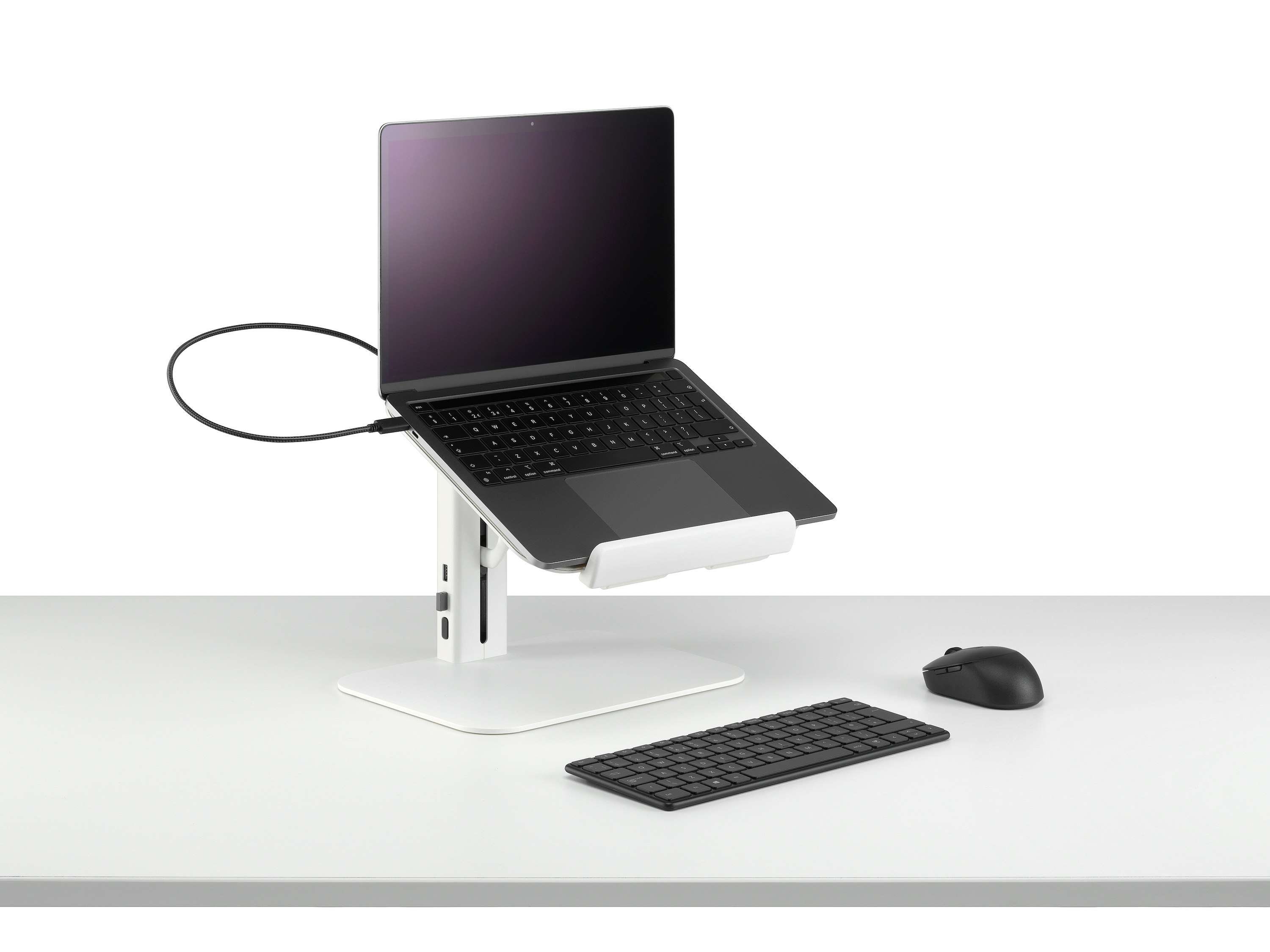 Lana laptop stand with laptop keyboard and mouse in white viewed from a sided angle.