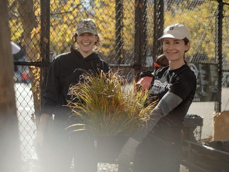Two smiling women carrying a potted plant while volunteering during MillerKnoll Day of Purpose.