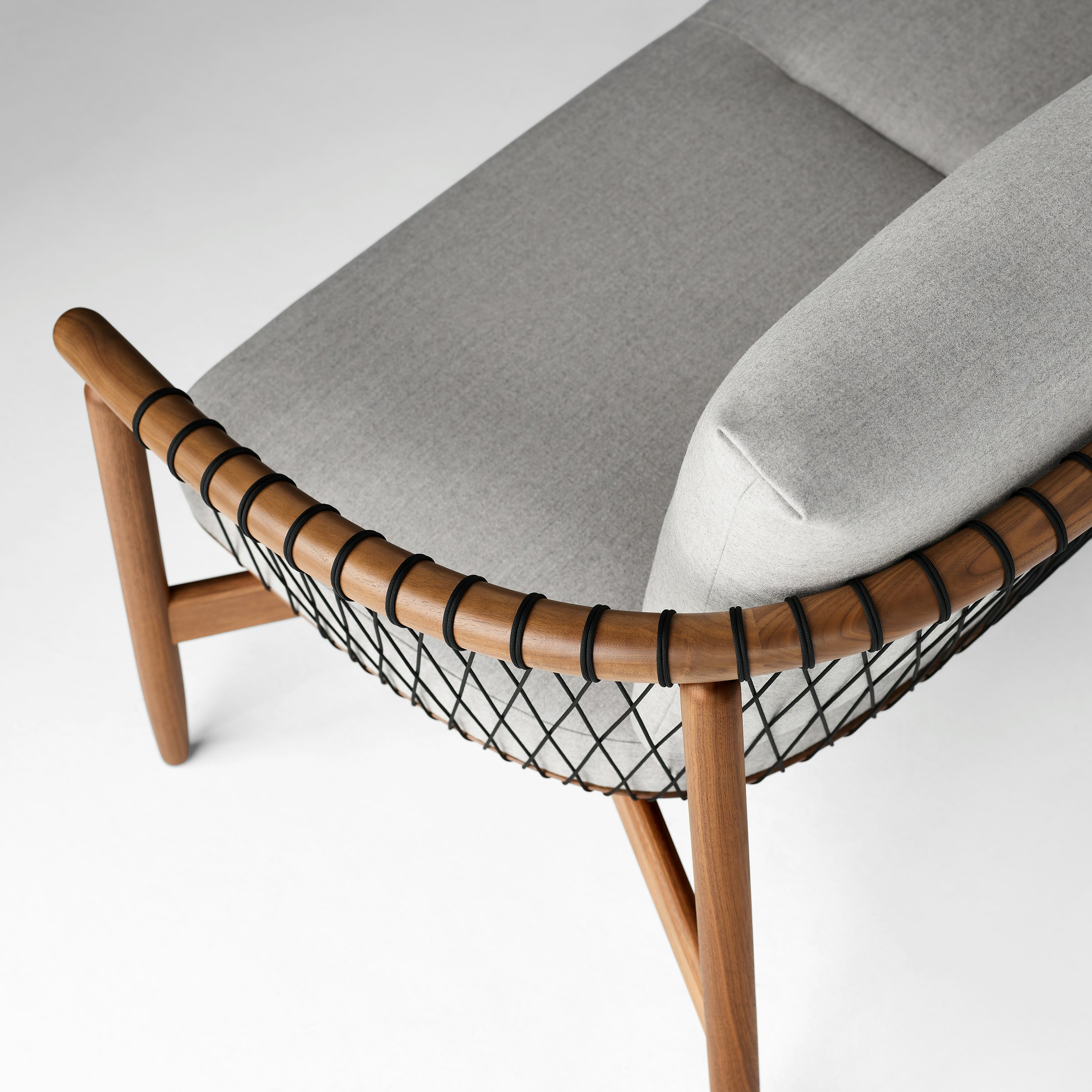 A detailed shot of a Crosshatch Settee with a walnut frame, black cords, and light neutral fabric. Viewed from the back at an angle.