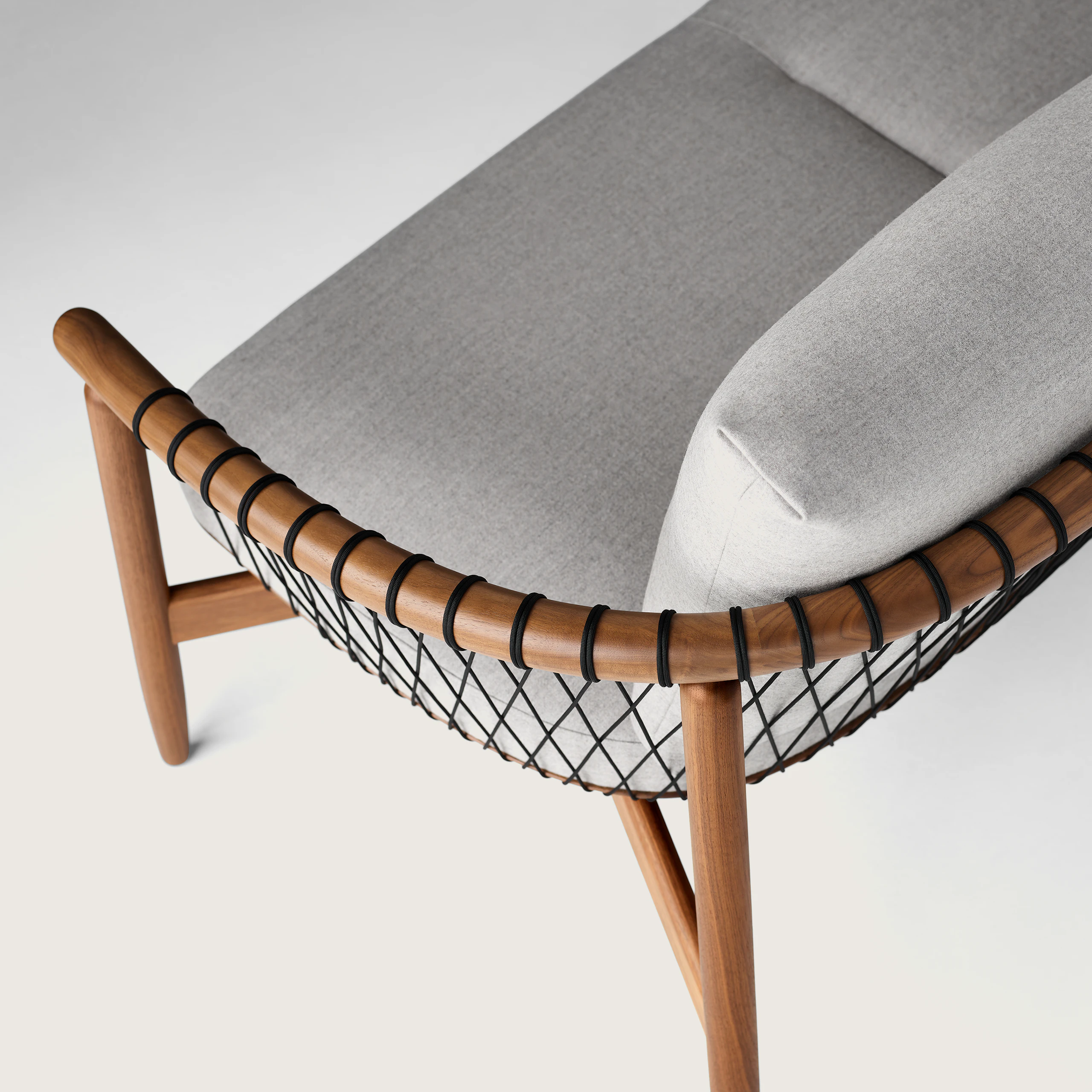 A detailed shot of a Crosshatch Settee with a walnut frame, black cords, and light neutral fabric. Viewed from the back at an angle.