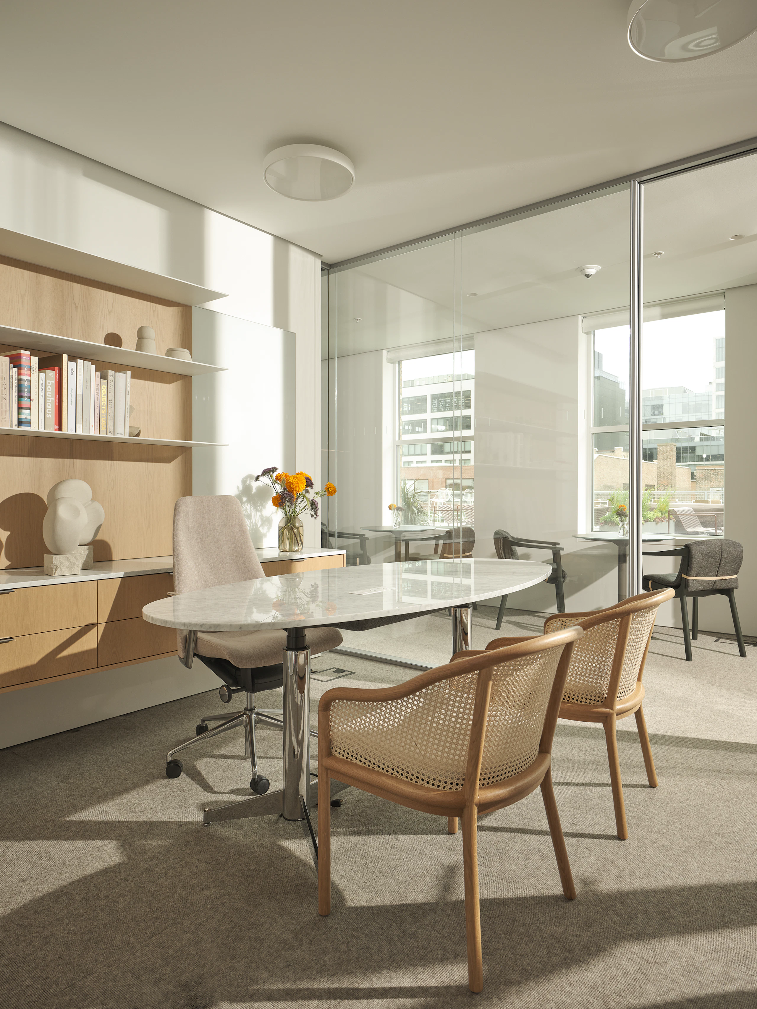 Private Office with a Geiger One Casegoods workwall in Nordic Oak, MP Height Adjustable Table in White Carrara Marble, Taper Chair, and two Landmark Chairs, viewed at an angle.