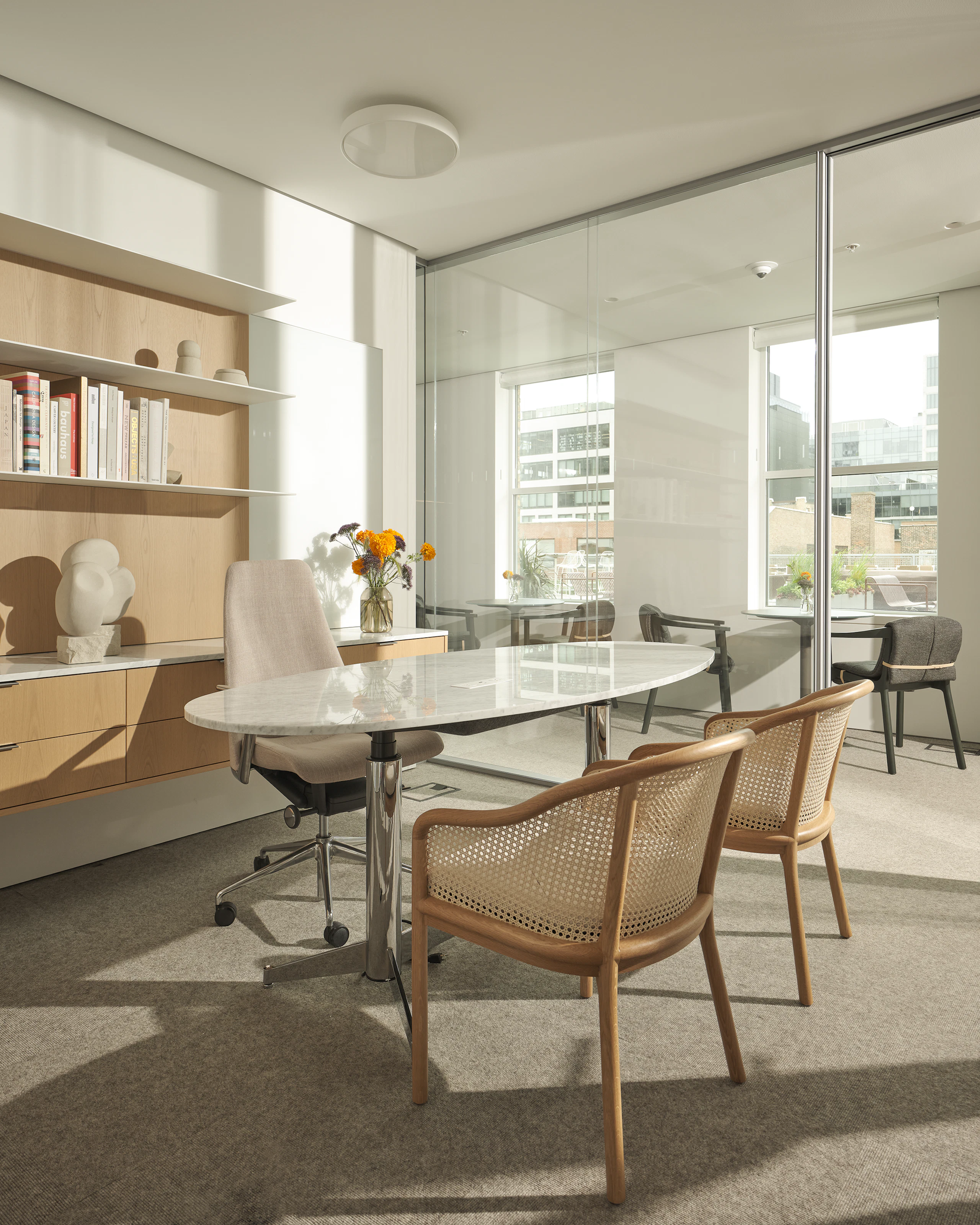 Private Office with a Geiger One Casegoods workwall in Nordic Oak, MP Height Adjustable Table in White Carrara Marble, Taper Chair, and two Landmark Chairs, viewed at an angle.