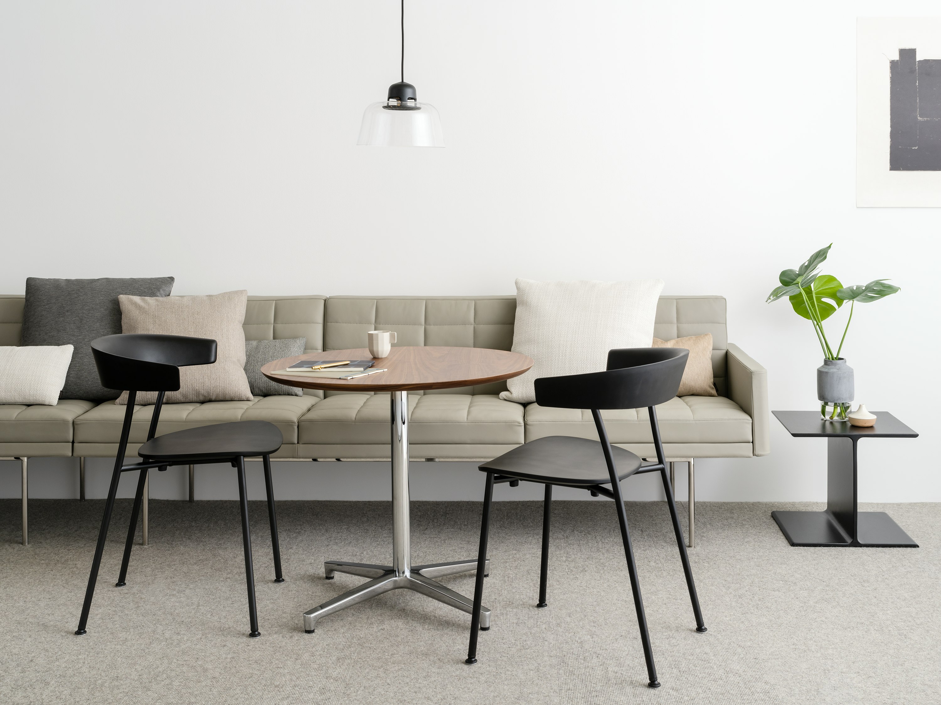 An informal meeting space featuring a tan Tuxedo Component sofa, a round Saiba occasional table, and two black Leeway side chairs.