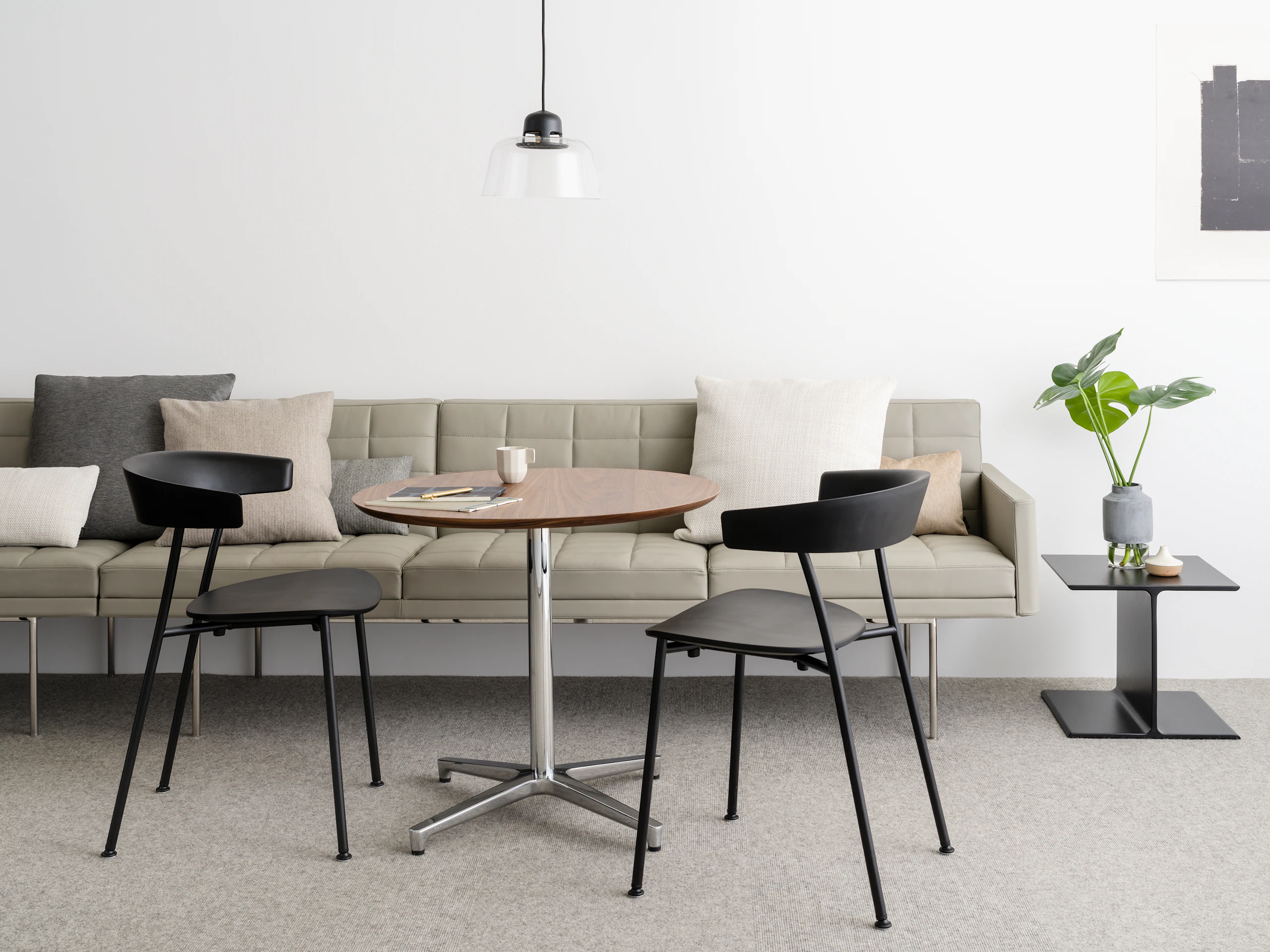 An informal meeting space featuring a tan Tuxedo Component sofa, a round Saiba occasional table, and two black Leeway side chairs.