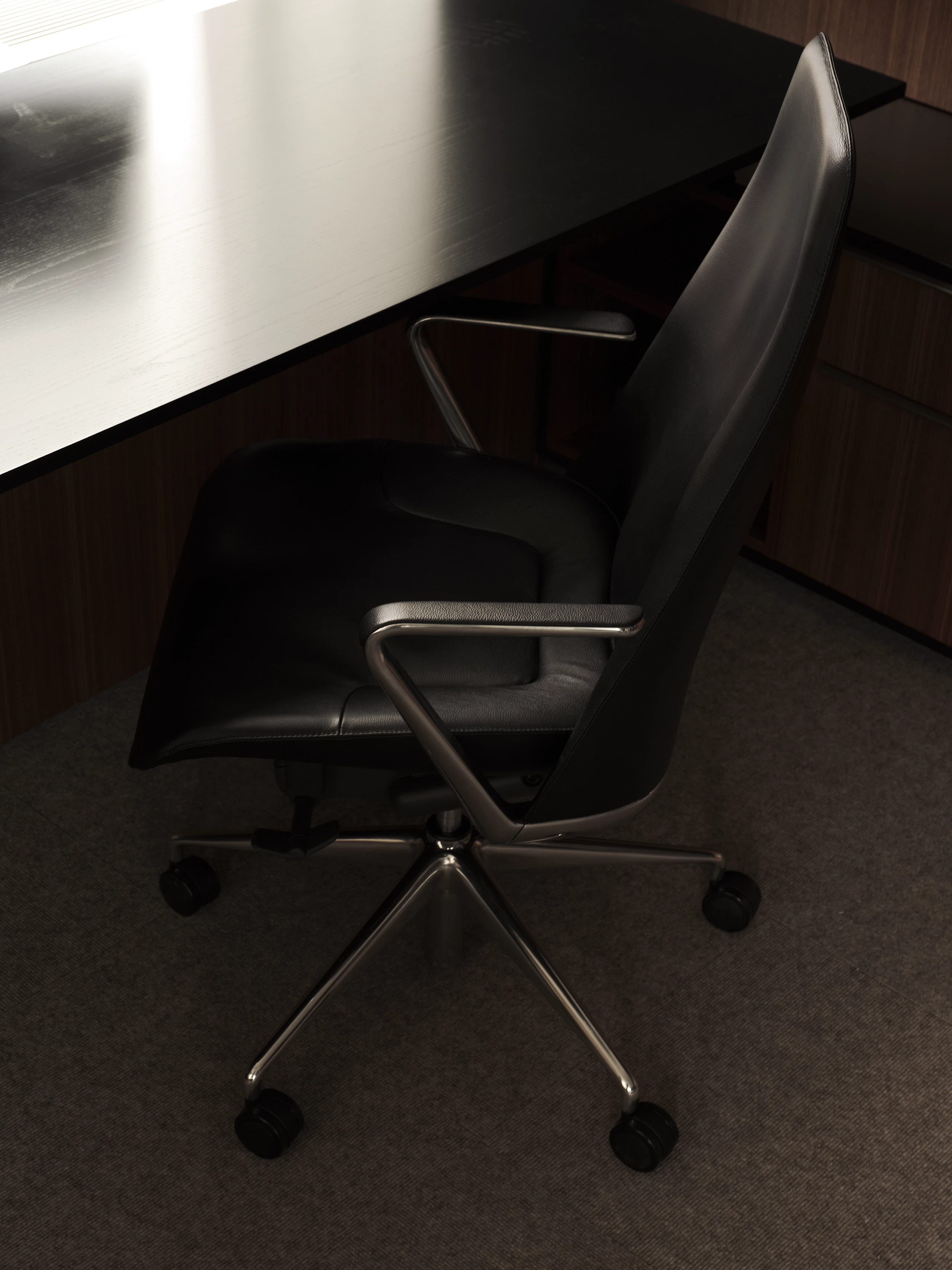 Taper Chair upholstered with black leather with a polished aluminum base next to a work surface in Ebonized Flat Cut Ash, viewed from above at an angle.