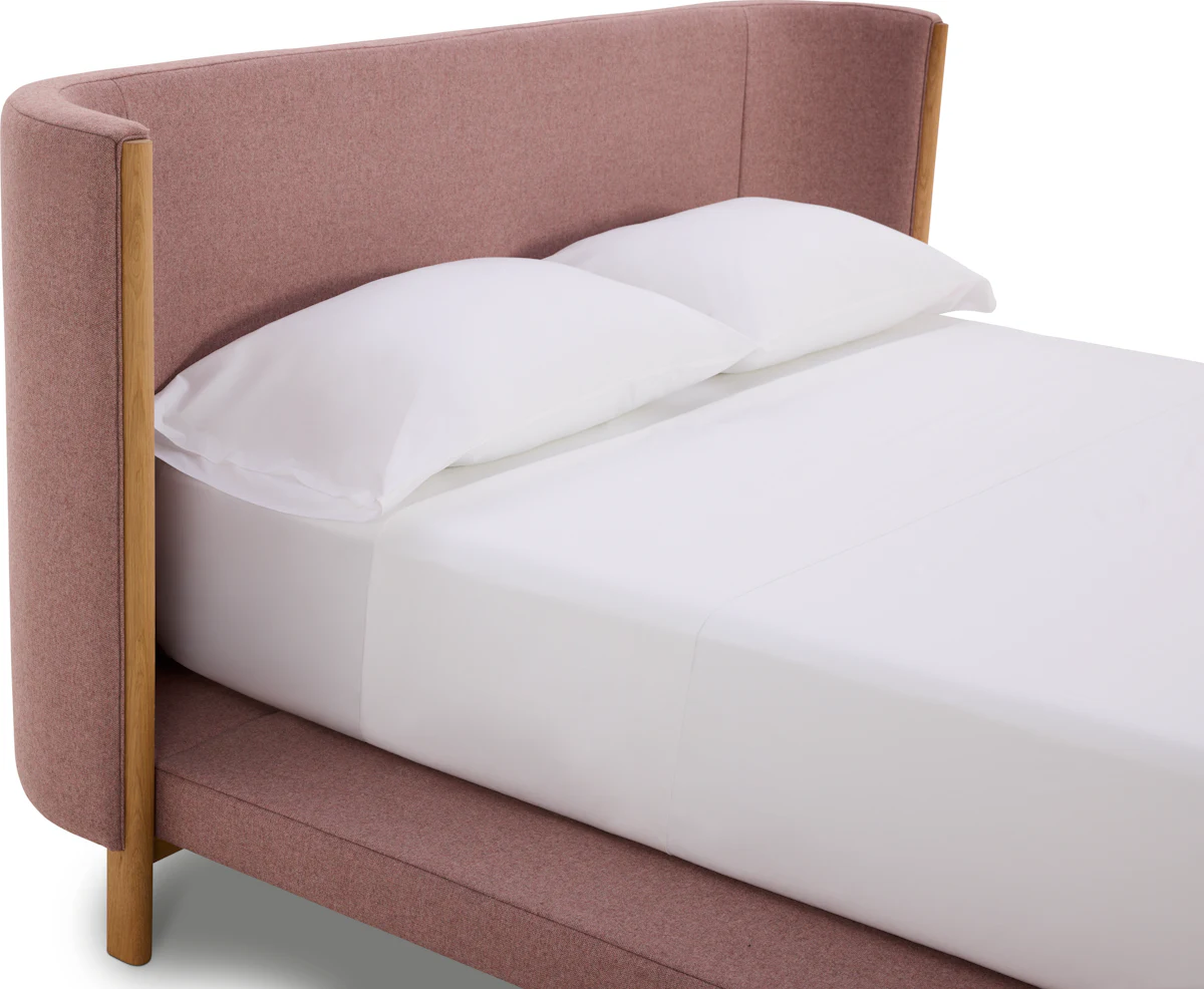 Pink upholstered bed with white sheets and wooden legs.