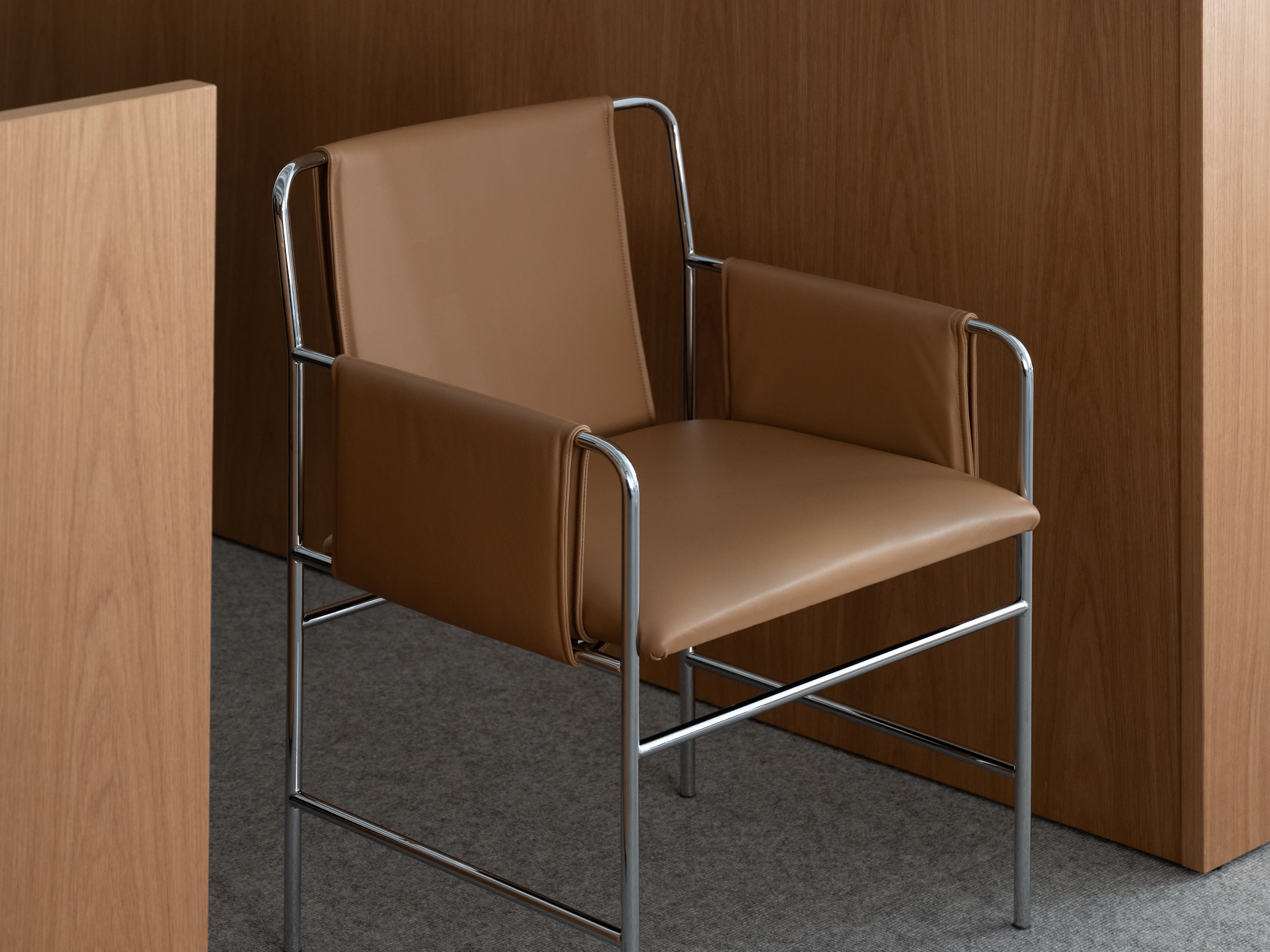 Envelope Chair upholstered with Bristol Leather in Camel with a Chrome Base beside viewed at an angle.