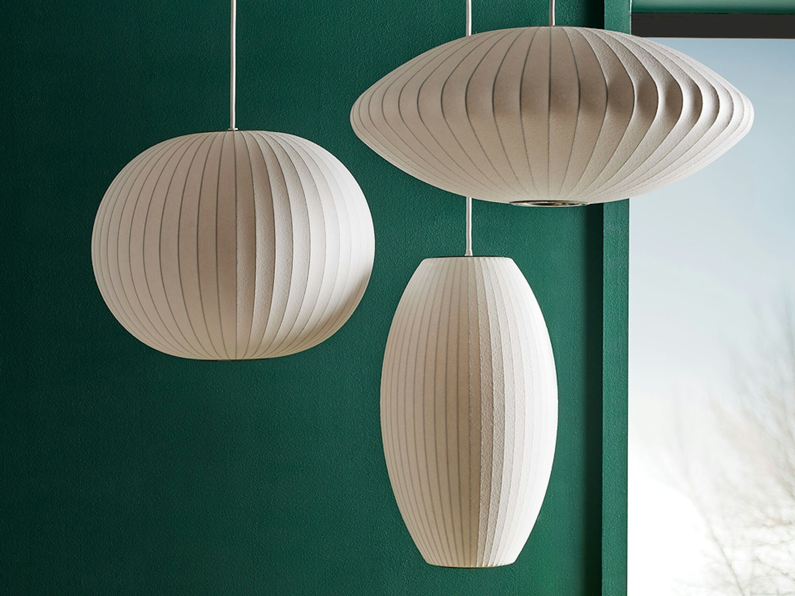 A Nelson Ball Pendant Lamp, Nelson Cigar Bubble Pendant, and Nelson Saucer Bubble Pendant hanging in front of a green wall