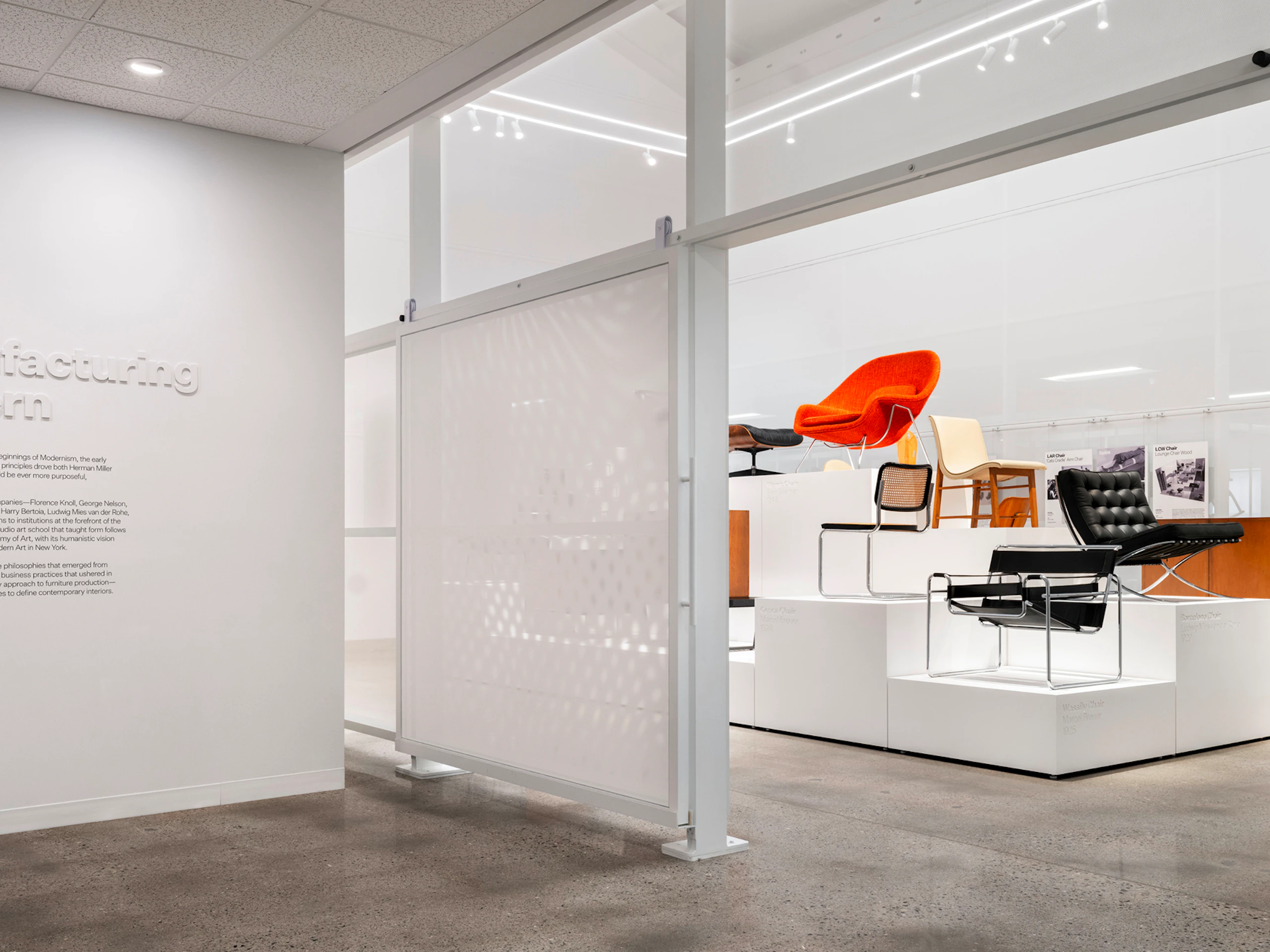 The entryway to the Manufacturing Modern exhibit at the MillerKnoll Archives with iconic furniture pieces, such as the Knoll Womb Chair and Barcelona Chair, on display in the background