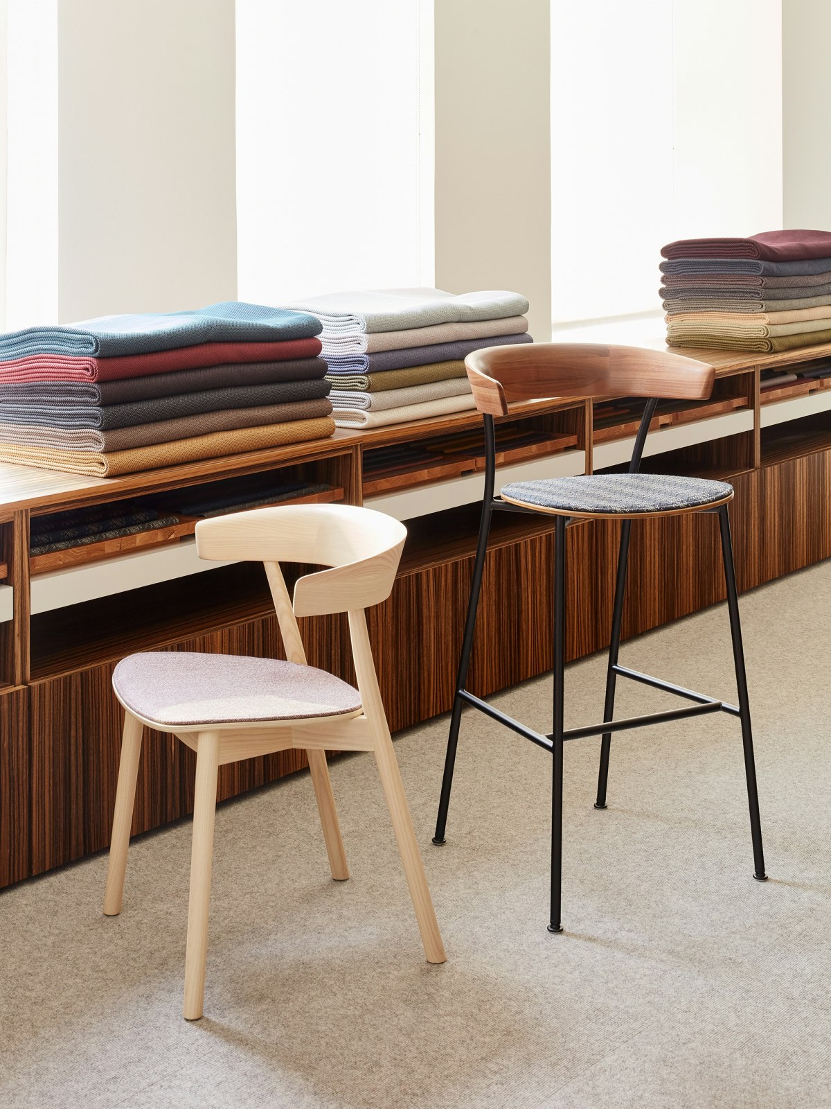 A Leeway Chair and a Leeway Stool sitting in front of a textile display featuring the Taconic Collection.