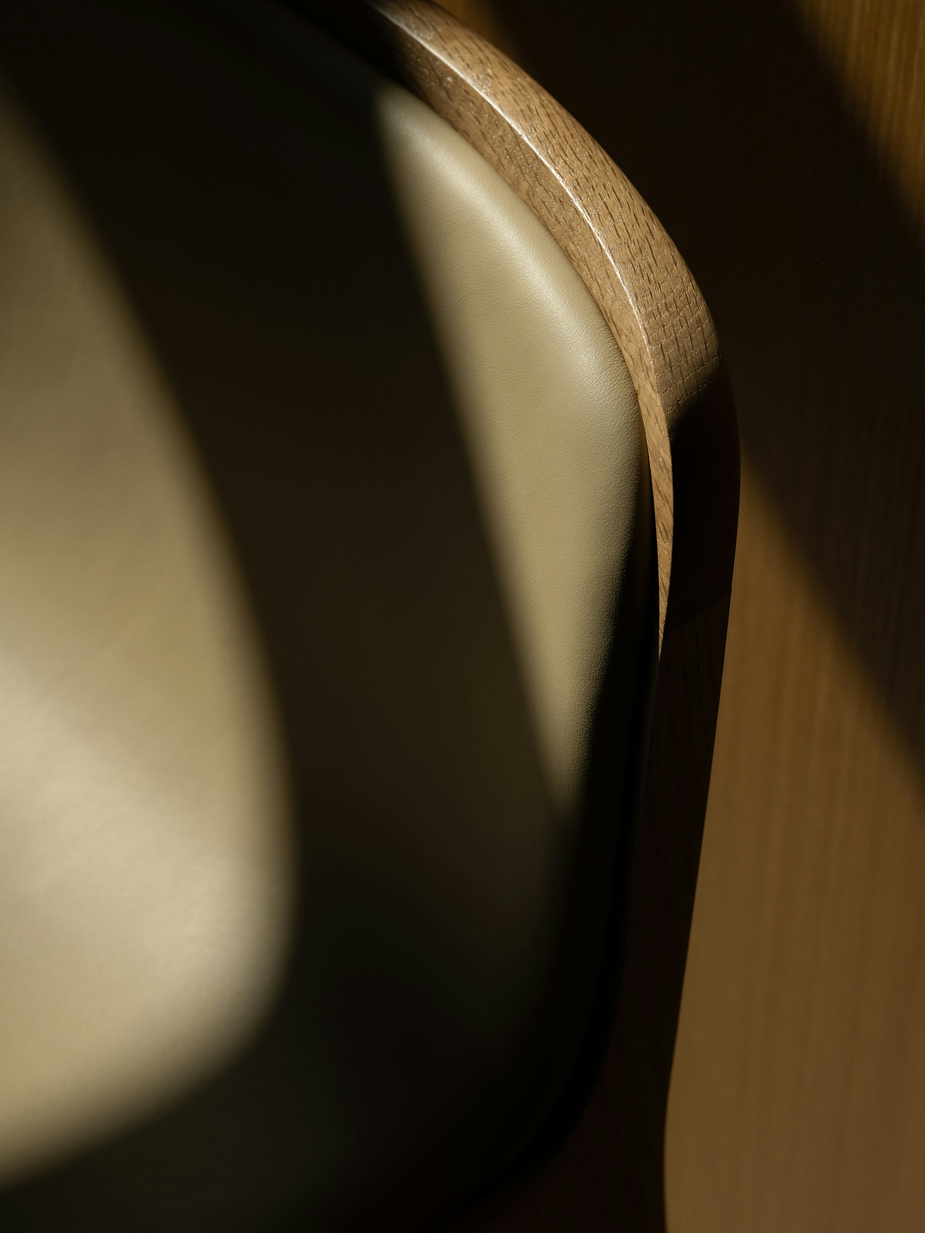 Detail view of a Lijn Stool backrest in Natural Oak fully upholstered with Bristol leather in Champagne, viewed from above.