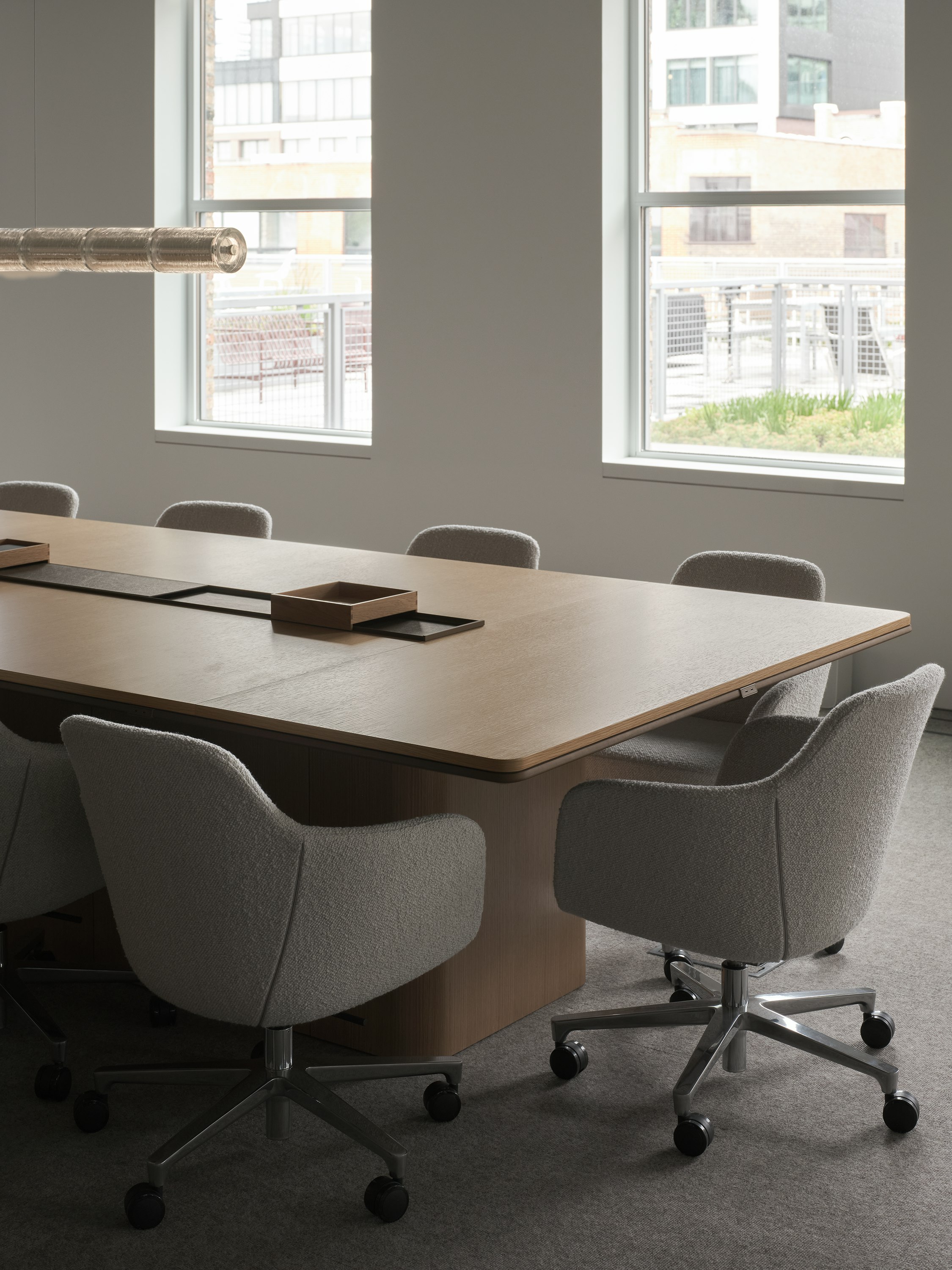 An Ascent Conference Table in Natural Rift Cut Oak with a plinth base surrounded by Saiba Conference Chairs upholstered with Pristina in Dove, viewed at an angle.