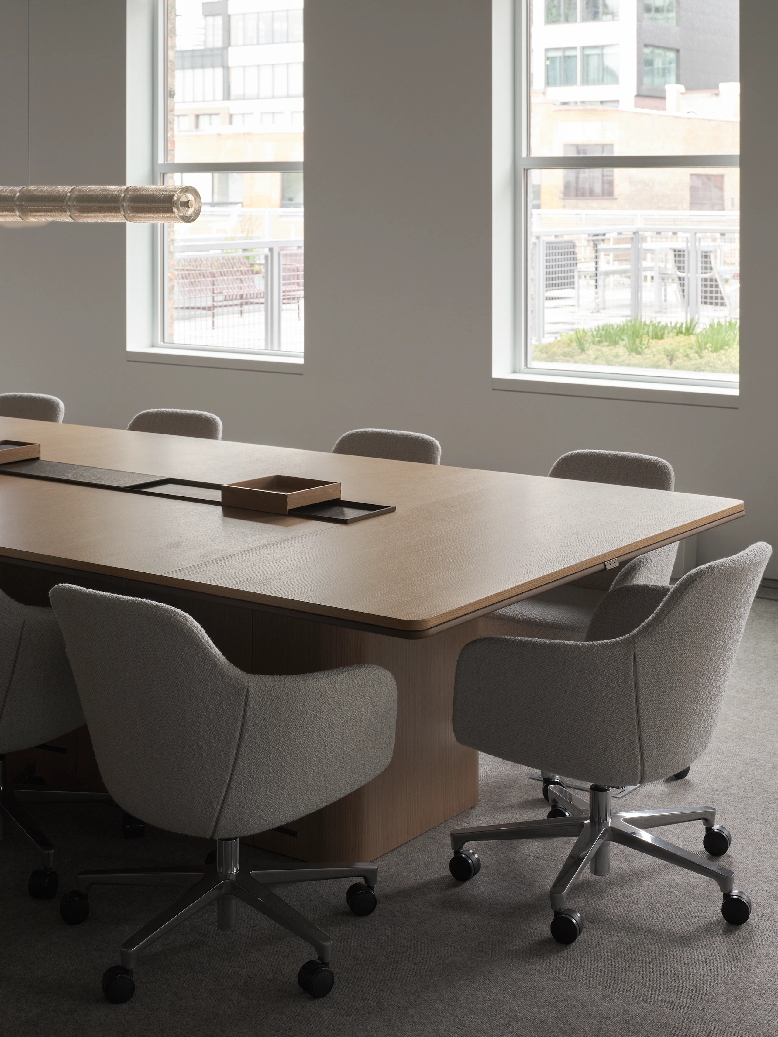 An Ascent Conference Table in Natural Rift Cut Oak with a plinth base surrounded by Saiba Conference Chairs upholstered with Pristina in Dove, viewed at an angle.