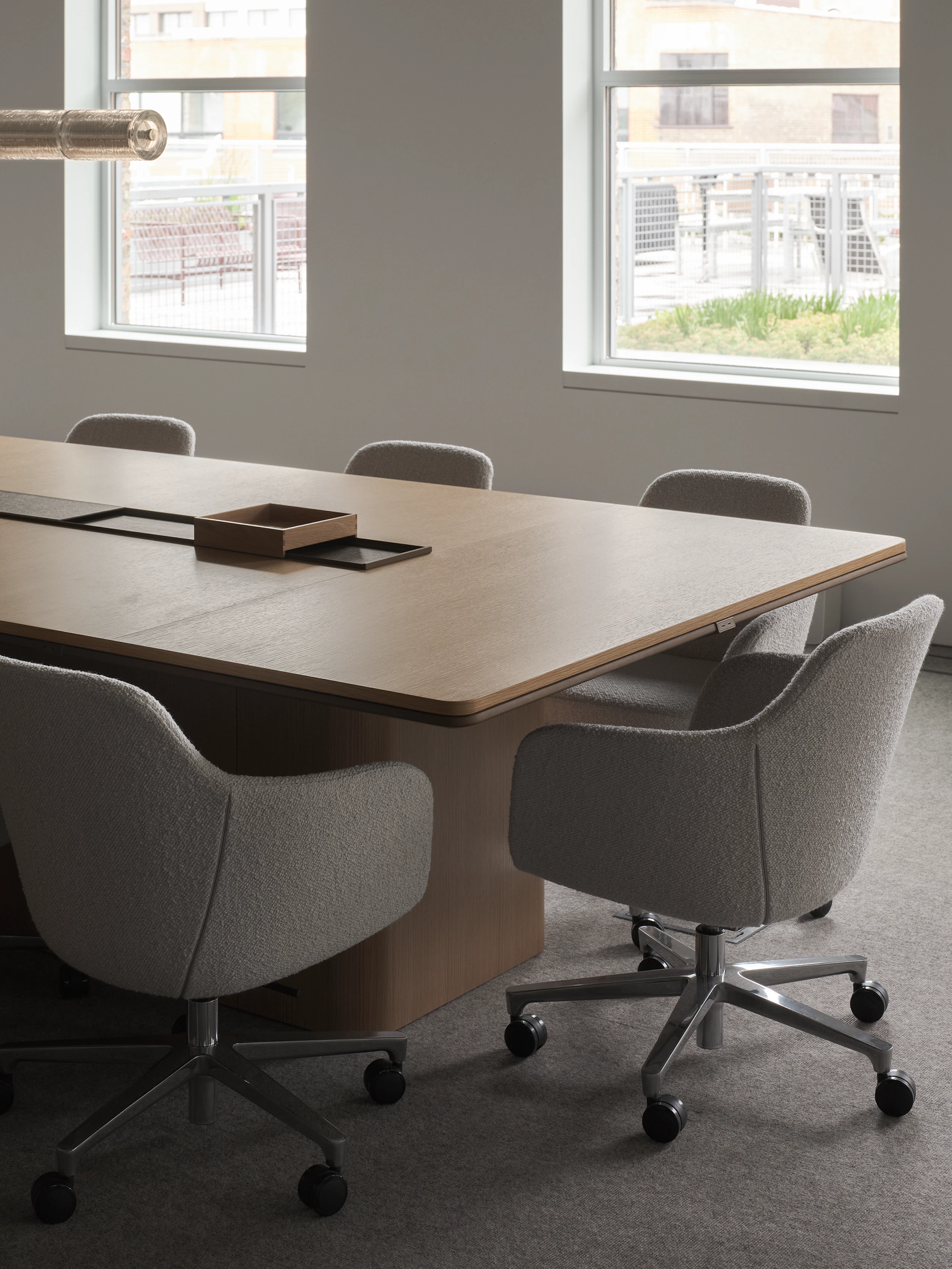 An Ascent Conference Table in Natural Rift Cut Oak with a plinth base surrounded by Saiba Conference Chairs upholstered with Pristina in Dove, viewed at an angle.
