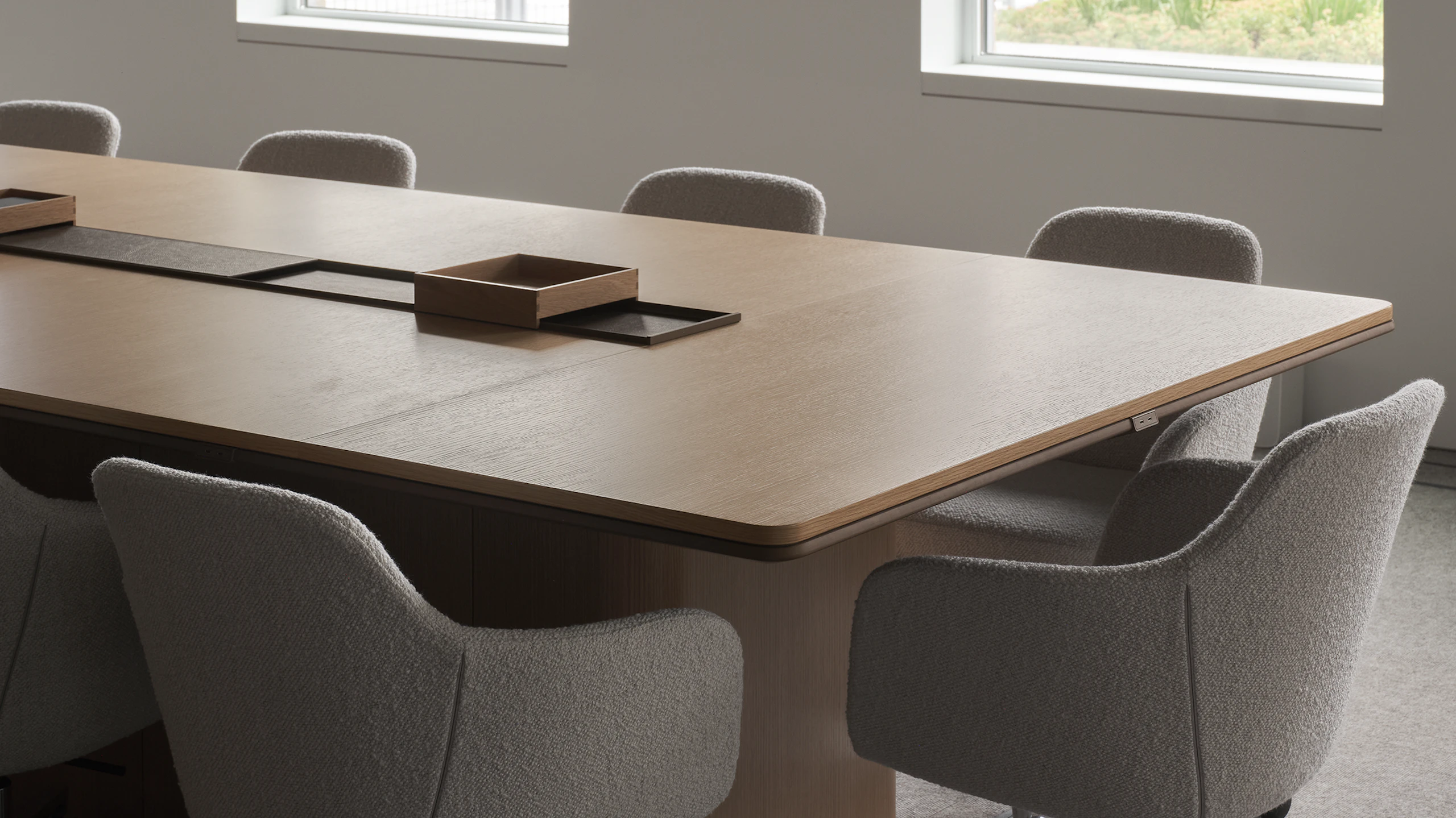 An Ascent Conference Table in Natural Rift Cut Oak with a plinth base surrounded by Saiba Conference Chairs upholstered with Pristina in Dove, viewed at an angle.