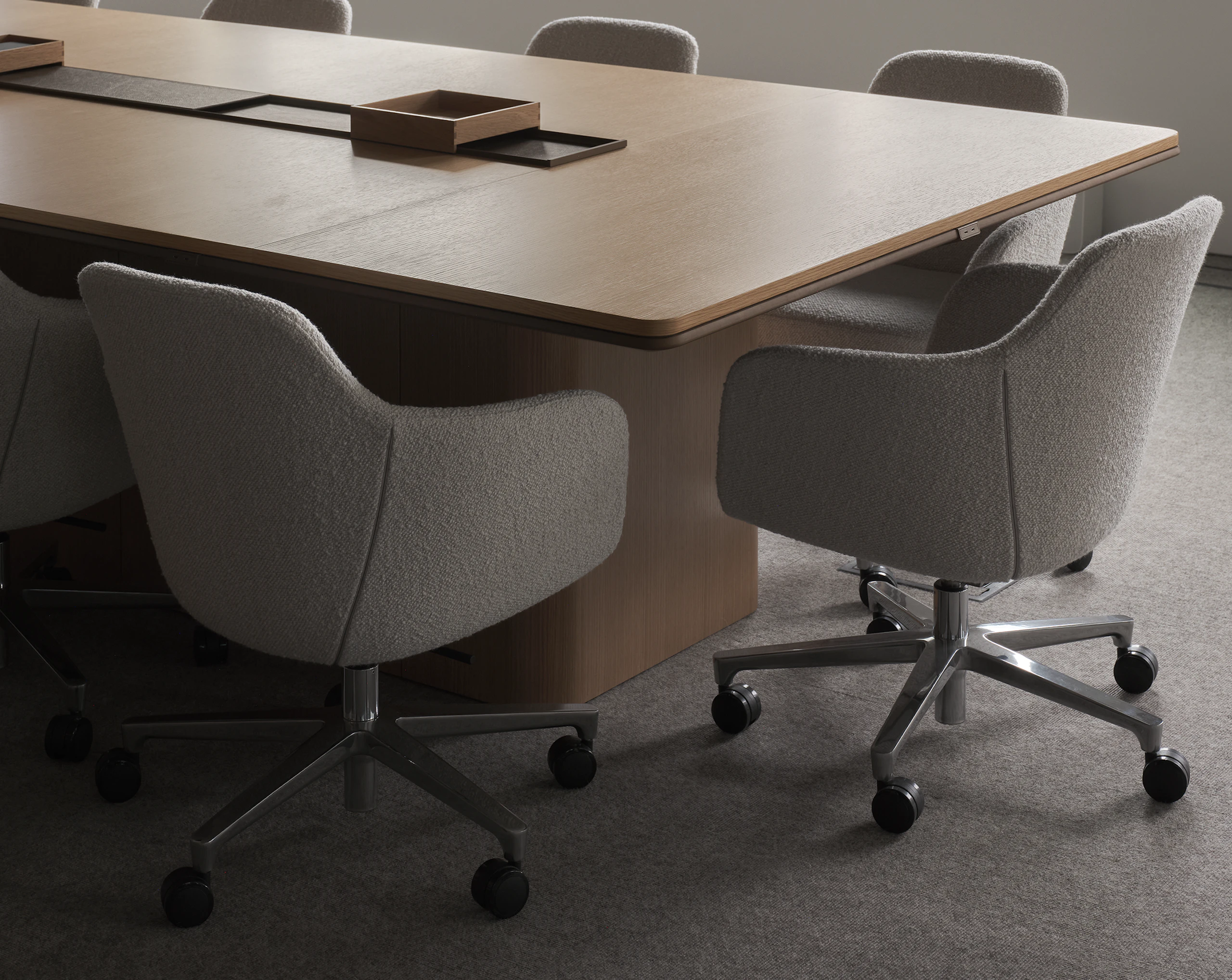 An Ascent Conference Table in Natural Rift Cut Oak with a plinth base surrounded by Saiba Conference Chairs upholstered with Pristina in Dove, viewed at an angle.