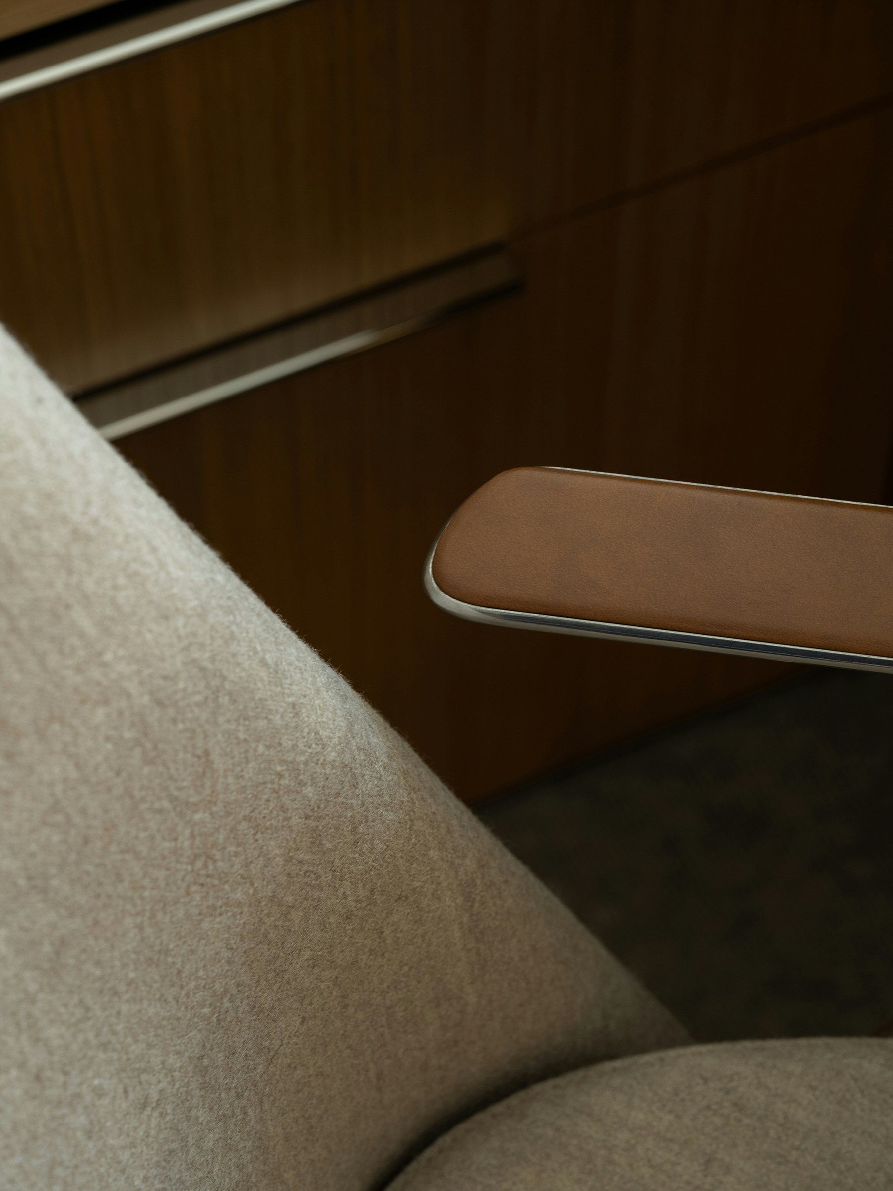 Detail view of a Taper Chair upholstered with Panno di Dolce in Dune with a polished aluminum frame and Bristol Leather armpads in Desert, viewed from above at an angle.