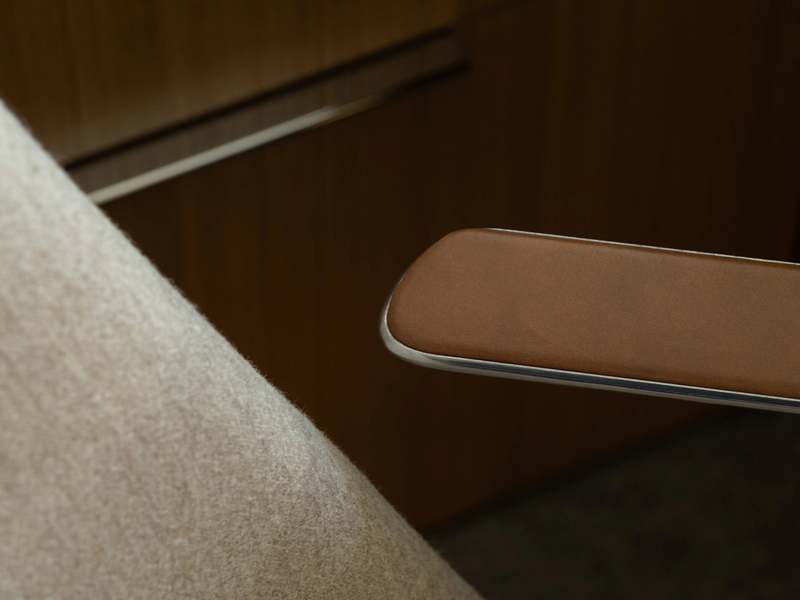 Detail view of a Taper Chair upholstered with Panno di Dolce in Dune with a polished aluminum frame and Bristol Leather armpads in Desert, viewed from above at an angle.