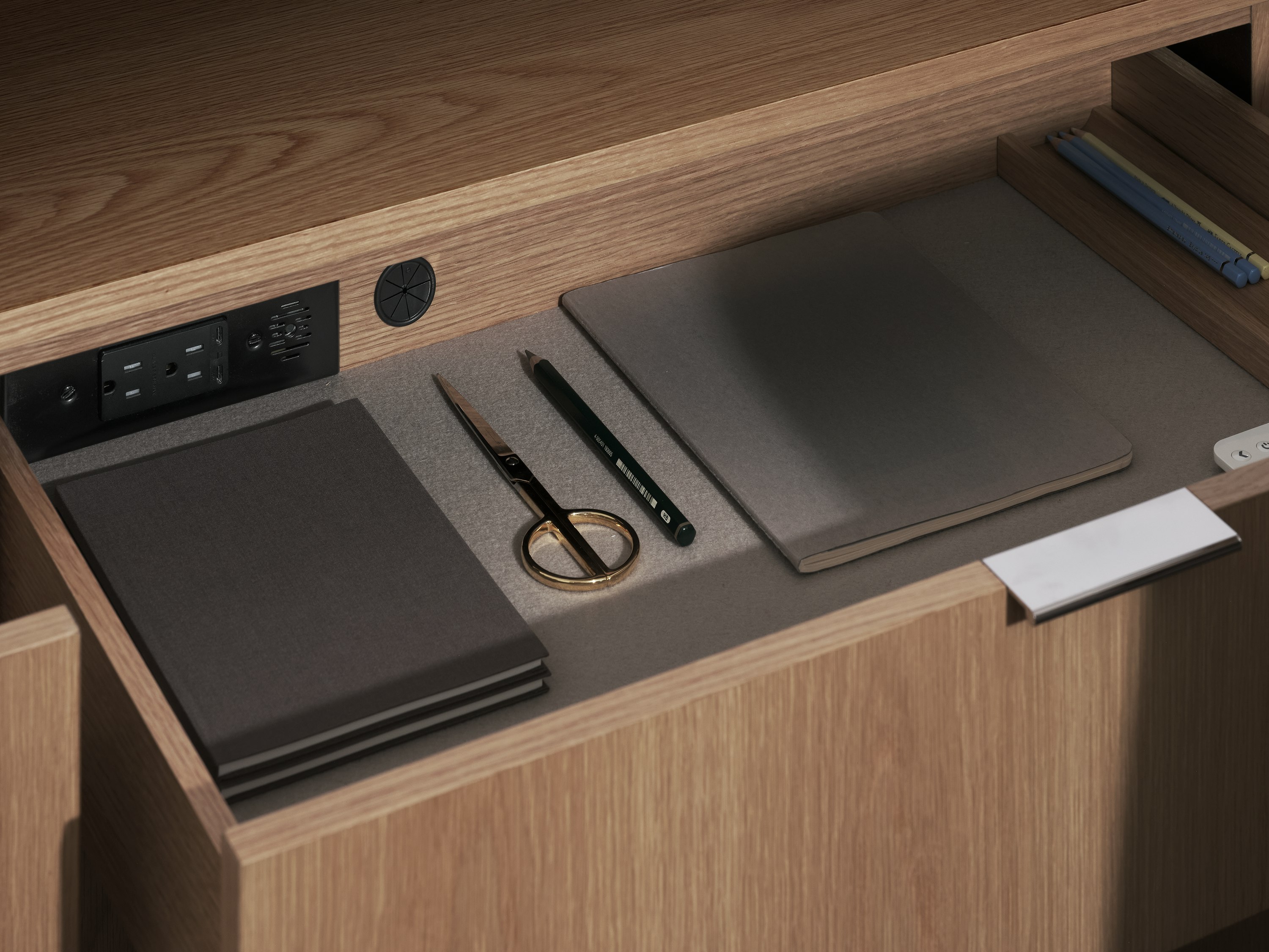 Detail view of an open felt-lined Geiger One Private Office storage drawer in Natural Flat Cut Oak with in-drawer power access, viewed at an angle.