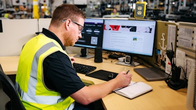 A person in a yellow safety vest writing on a notebook.