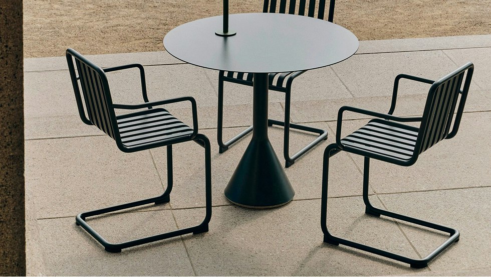 Three chairs and a matching table from the Palissade Cantilever collection from HAY on an outdoor patio.