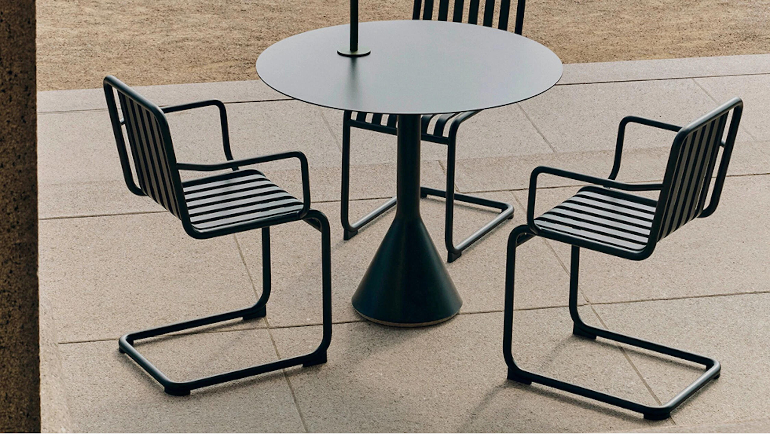 Three chairs and a matching table from the Palissade Cantilever collection from HAY on an outdoor patio.