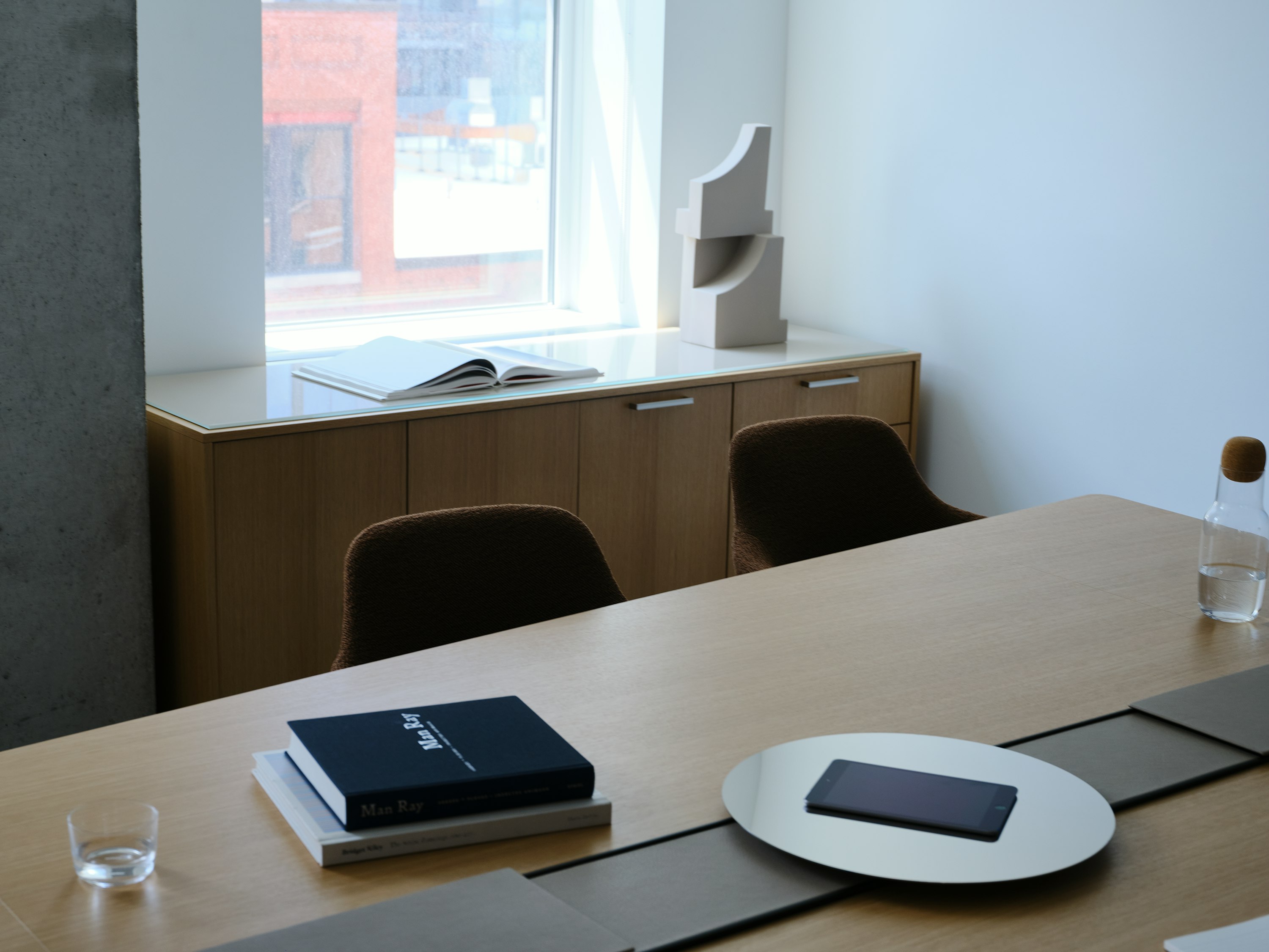 Ascent Conference Table designed by EOOS in Natural Rift Cut Oak with a leather-covered power trough and  chrome accessory tray, with Saiba Chairs and a JD Credenza, viewed at an angle in a conference room setting.
