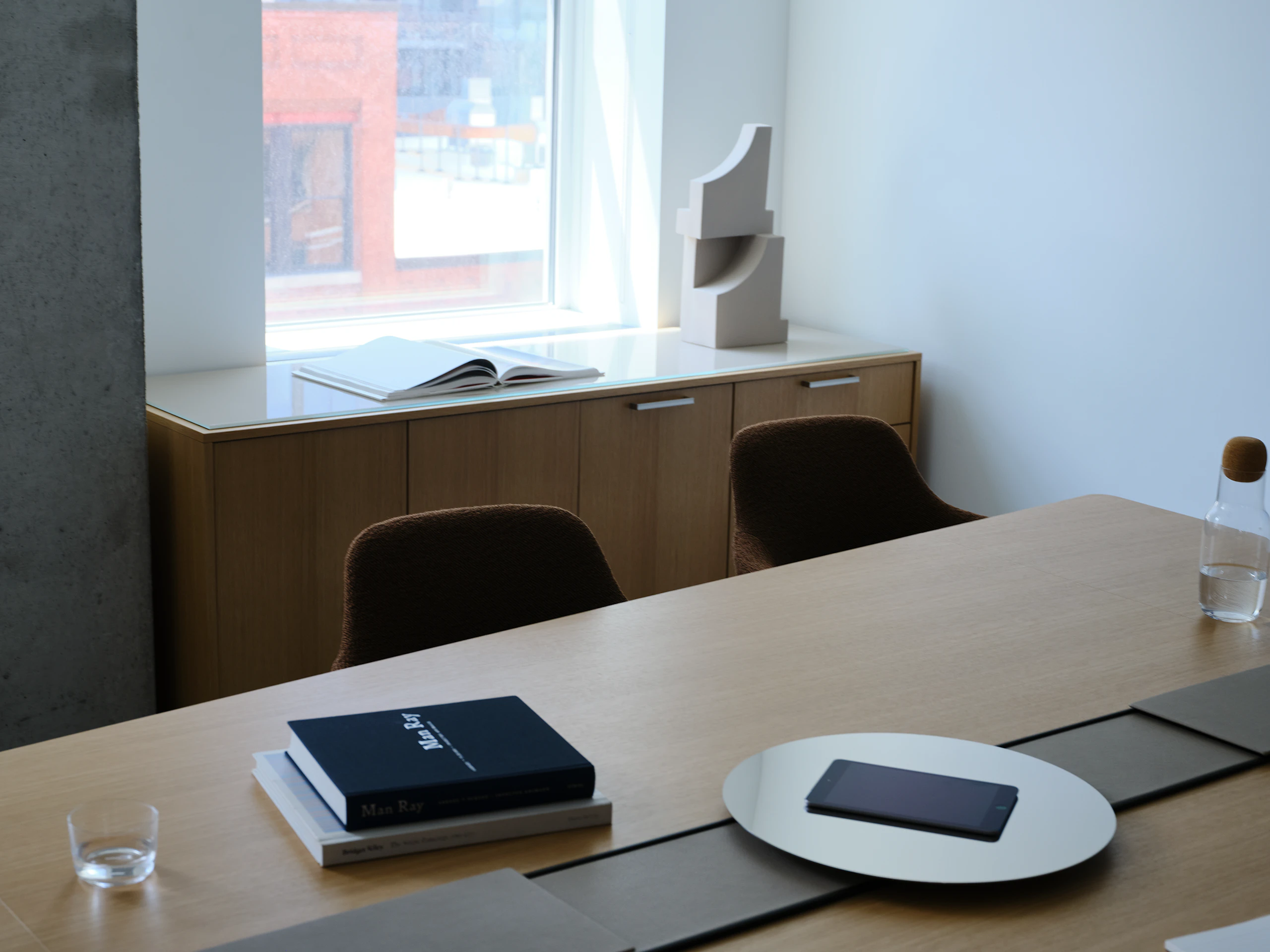 Ascent Conference Table designed by EOOS in Natural Rift Cut Oak with a leather-covered power trough and chrome accessory tray, with Saiba Chairs and a JD Credenza, viewed at an angle in a conference room setting.