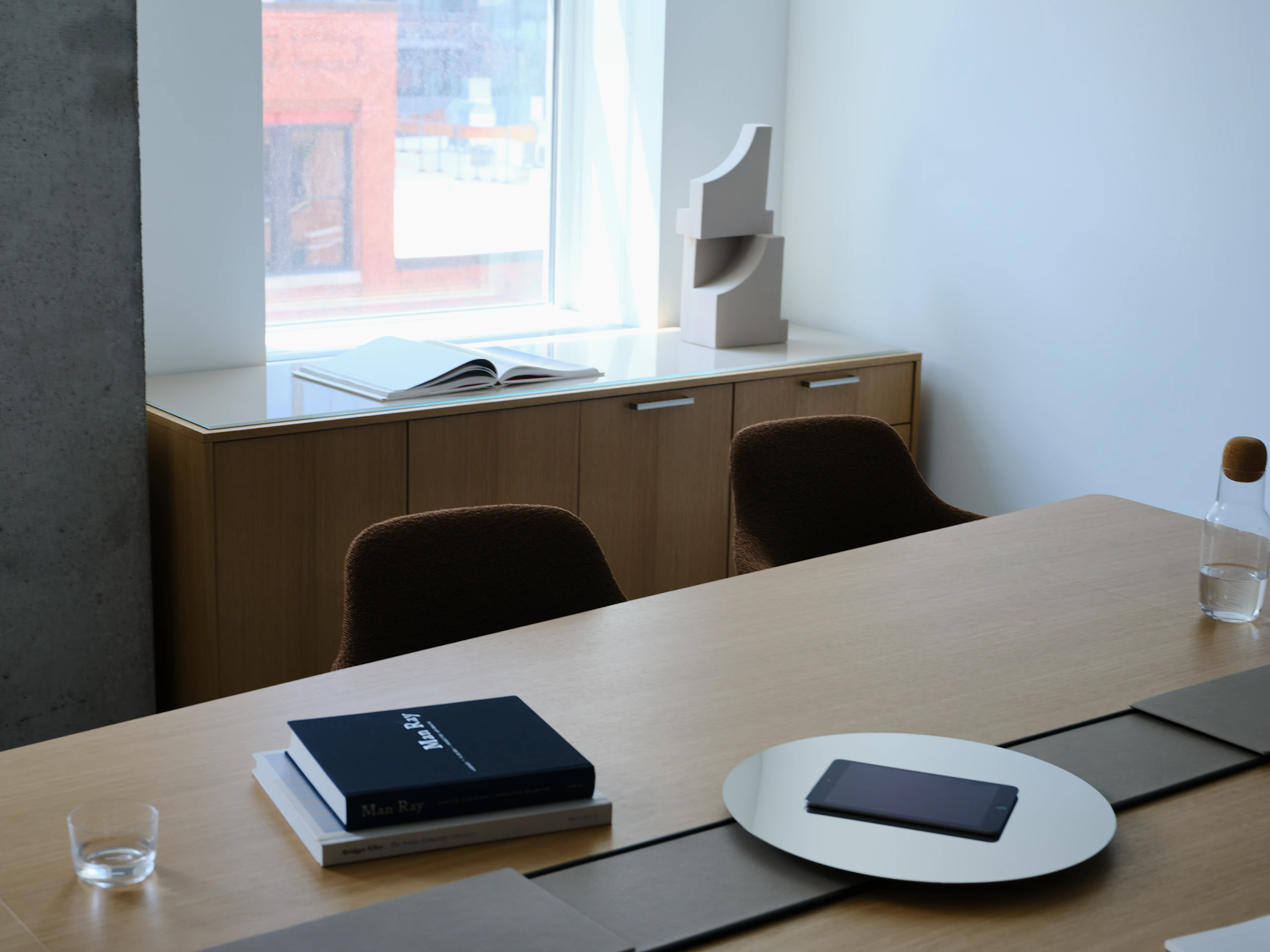 Ascent Conference Table designed by EOOS in Natural Rift Cut Oak with a leather-covered power trough and chrome accessory tray, with Saiba Chairs and a JD Credenza, viewed at an angle in a conference room setting.